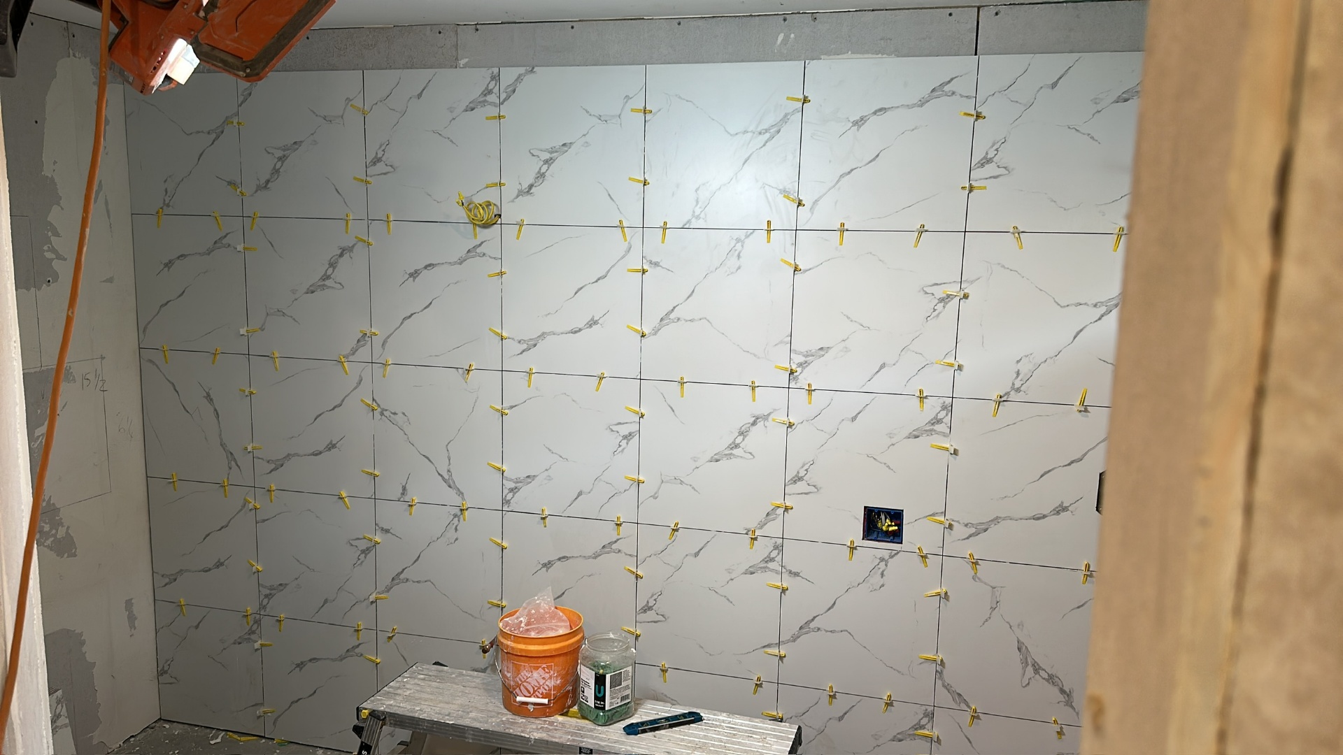 Side shower wall fully tiled with marble-look large-format porcelain and leveling clips still in place in Metairie master bath