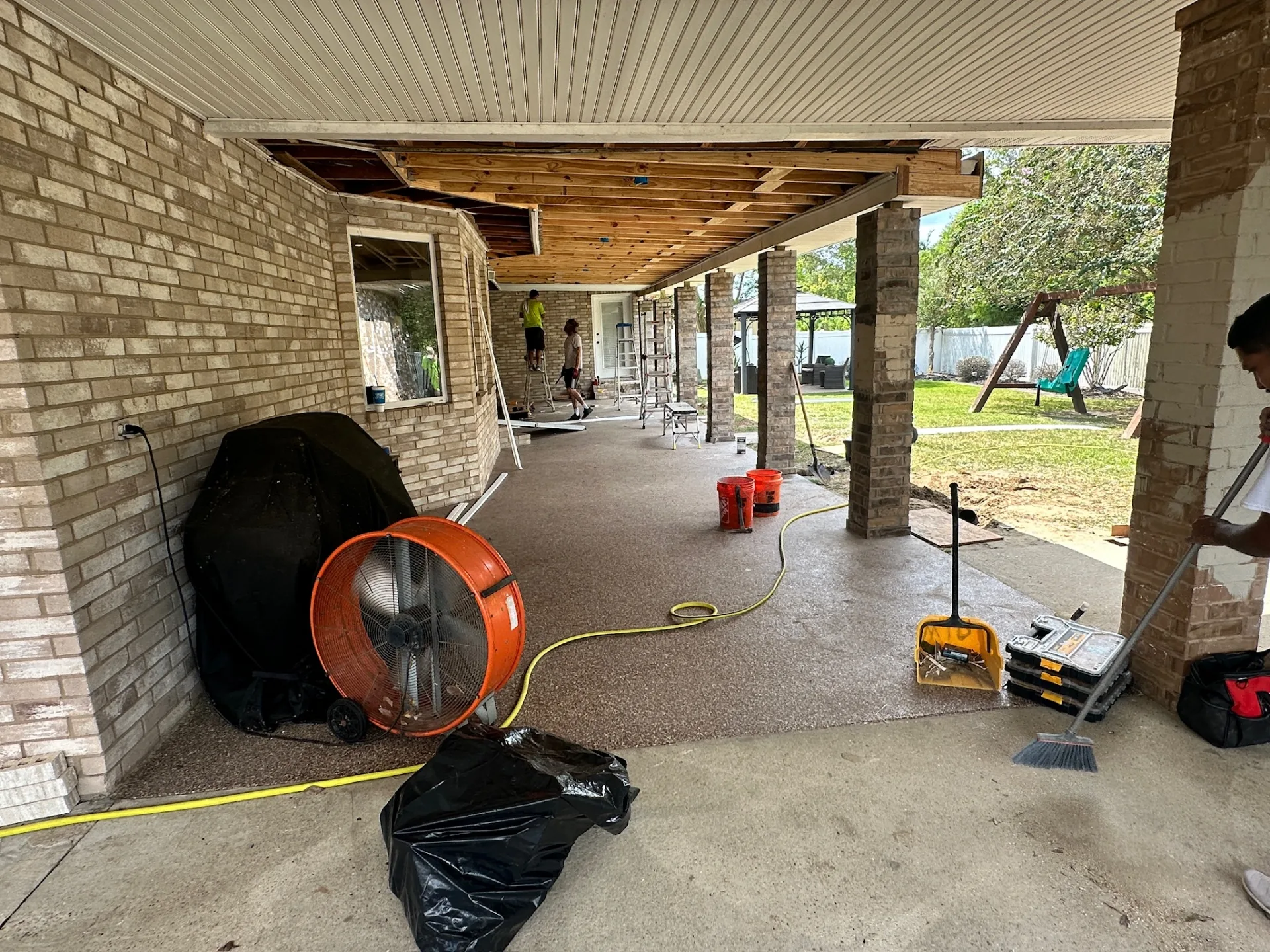 Long run view under rebuilt patio roof showing soffit panels being installed across Destrehan Louisiana home rear elevation