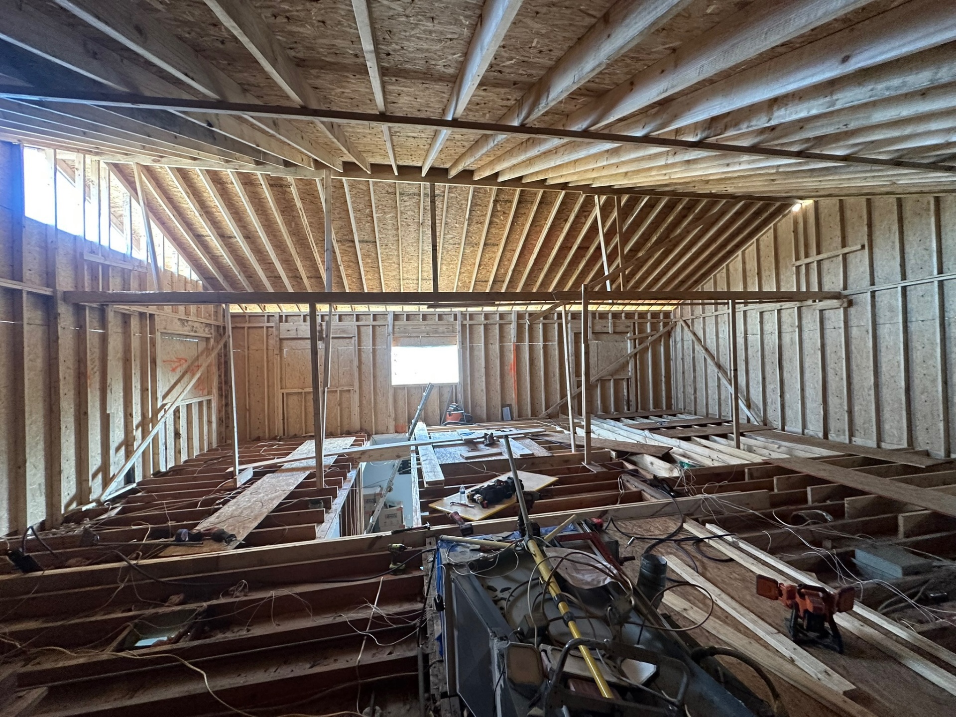 Inside Metairie attic looking up at new roof rafters and ridge framing installed directly above existing dark-stained ceiling joists and floor framing below