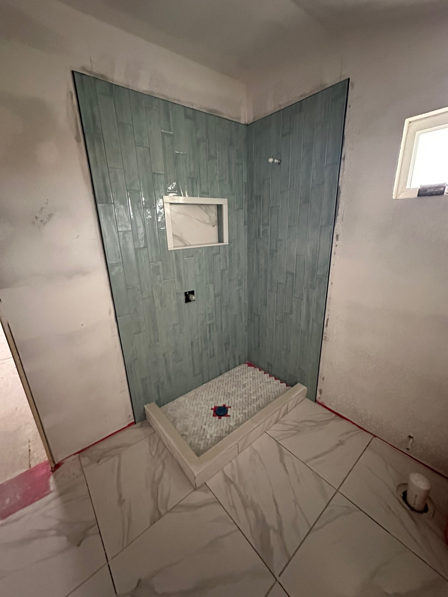 Completed shower tile in the Metairie second-floor master bath with sage-green vertical wall tile, a framed marble niche, marble herringbone mosaic shower pan and marble floor tile around the curb