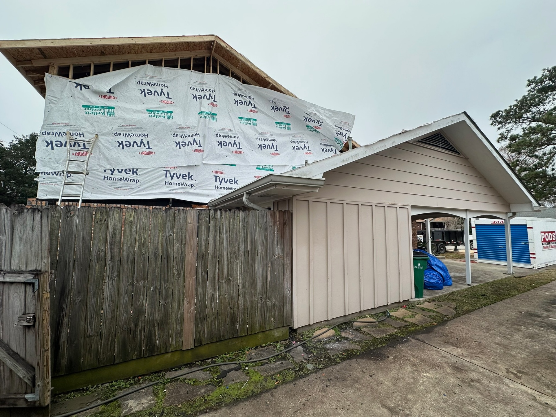 Side view of Metairie home addition with second floor fully wrapped in Tyvek alongside the original single-story carport for context