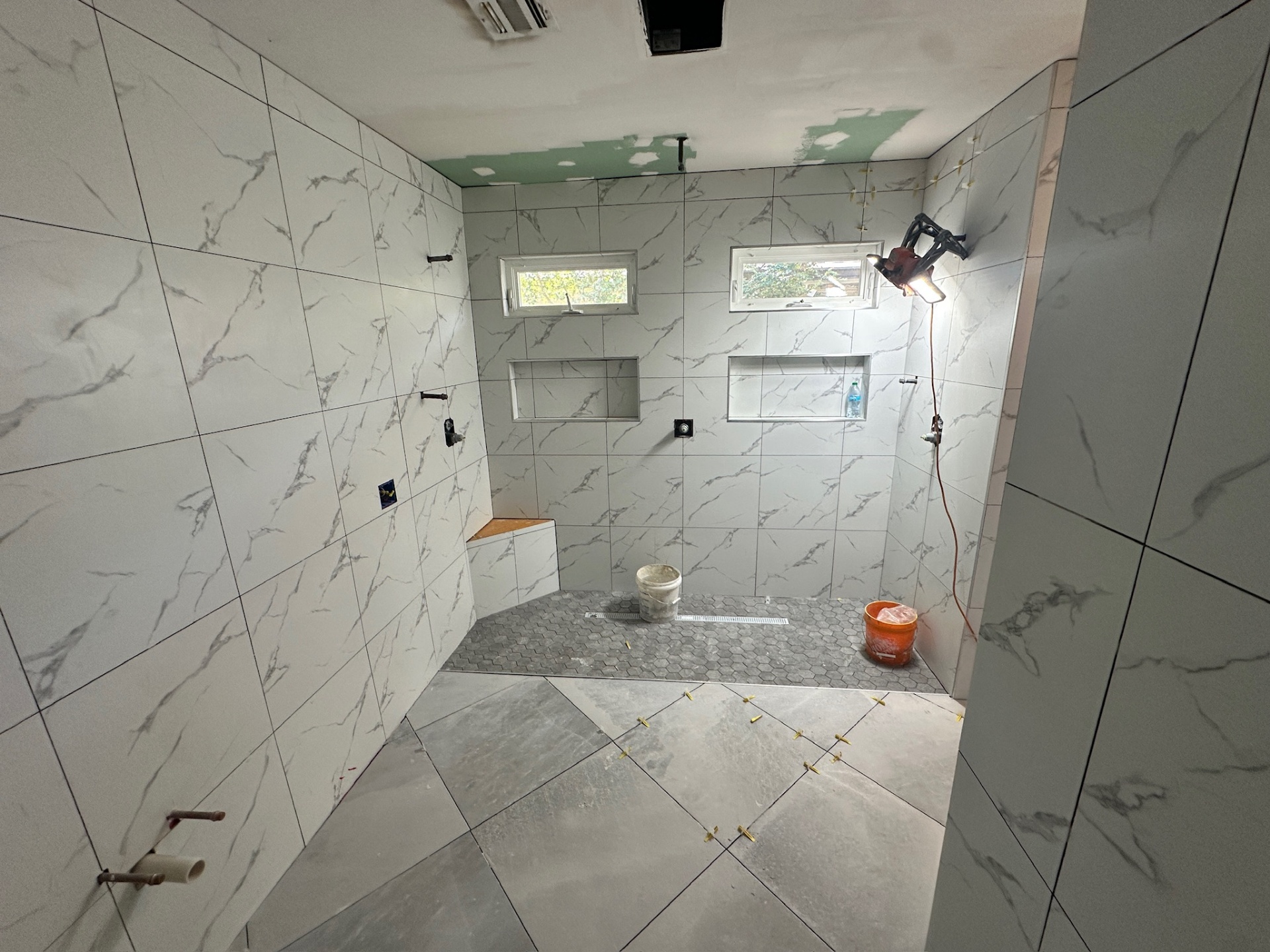 Wide walk-in shower mid-tile with dual niches, dual awning windows, and hex mosaic floor going down in Metairie master bath