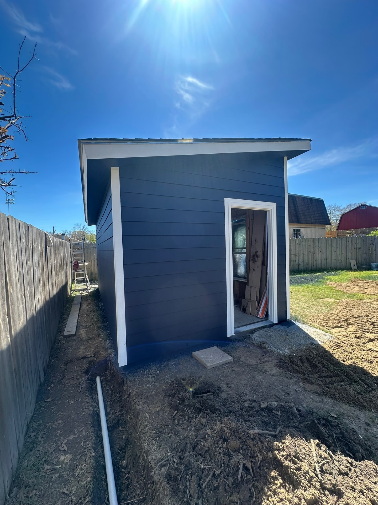 Rear side elevation of Metairie Hardie-siding shed with navy paint and white corner trim, drainage trench at fence line