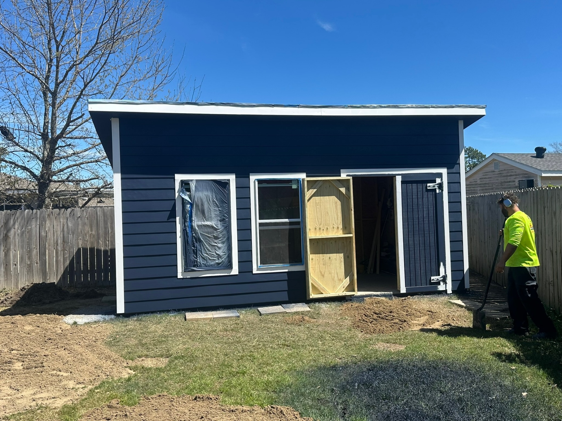 Crew member installing pressure-treated barn-style double doors on navy Hardie-siding shed in Metairie backyard