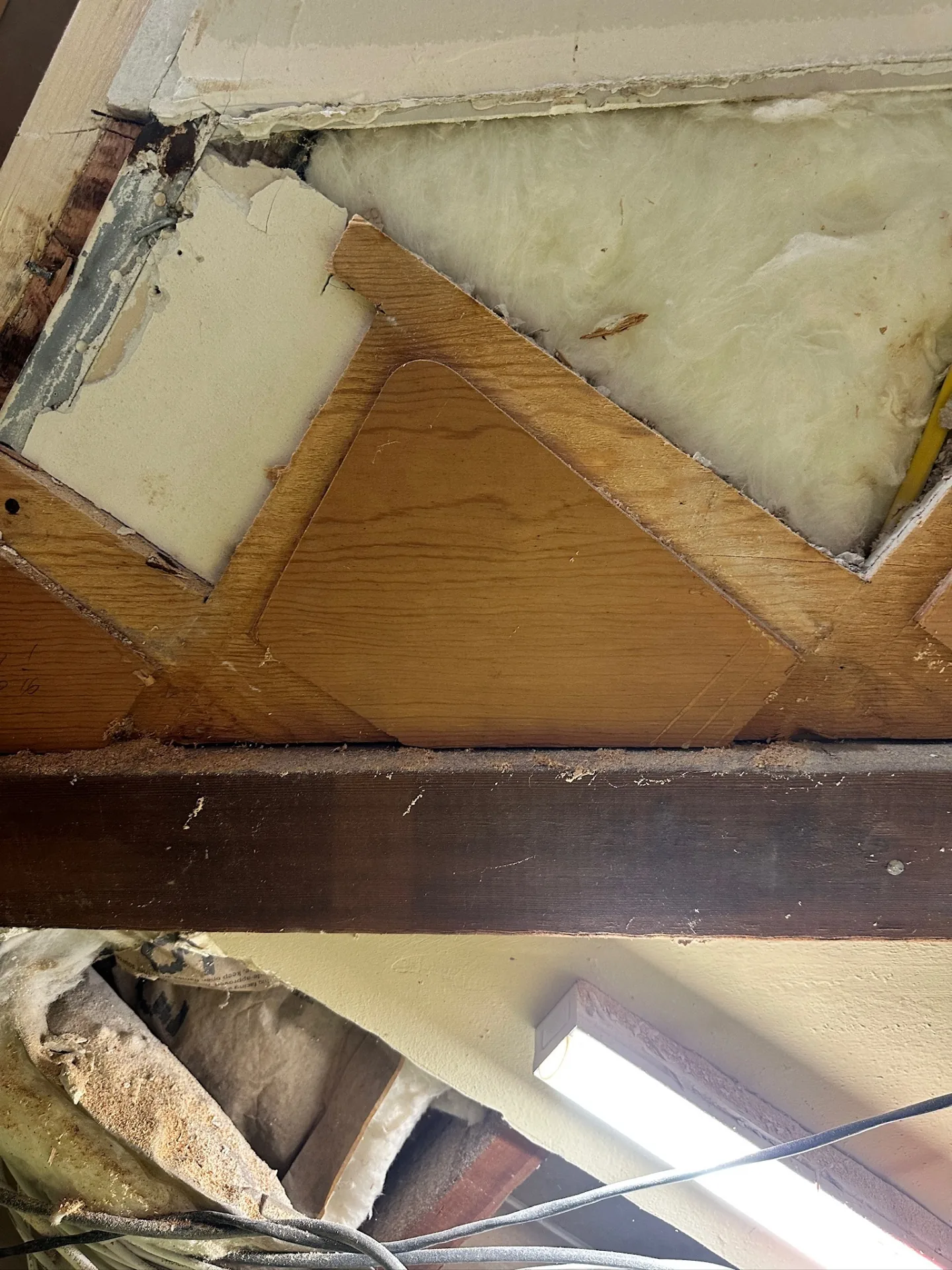Hidden framing damage discovered at the soffit during exploratory demo at Blanke Street Metairie home remodel, with old plywood gussets, insulation, and beam pocket exposed