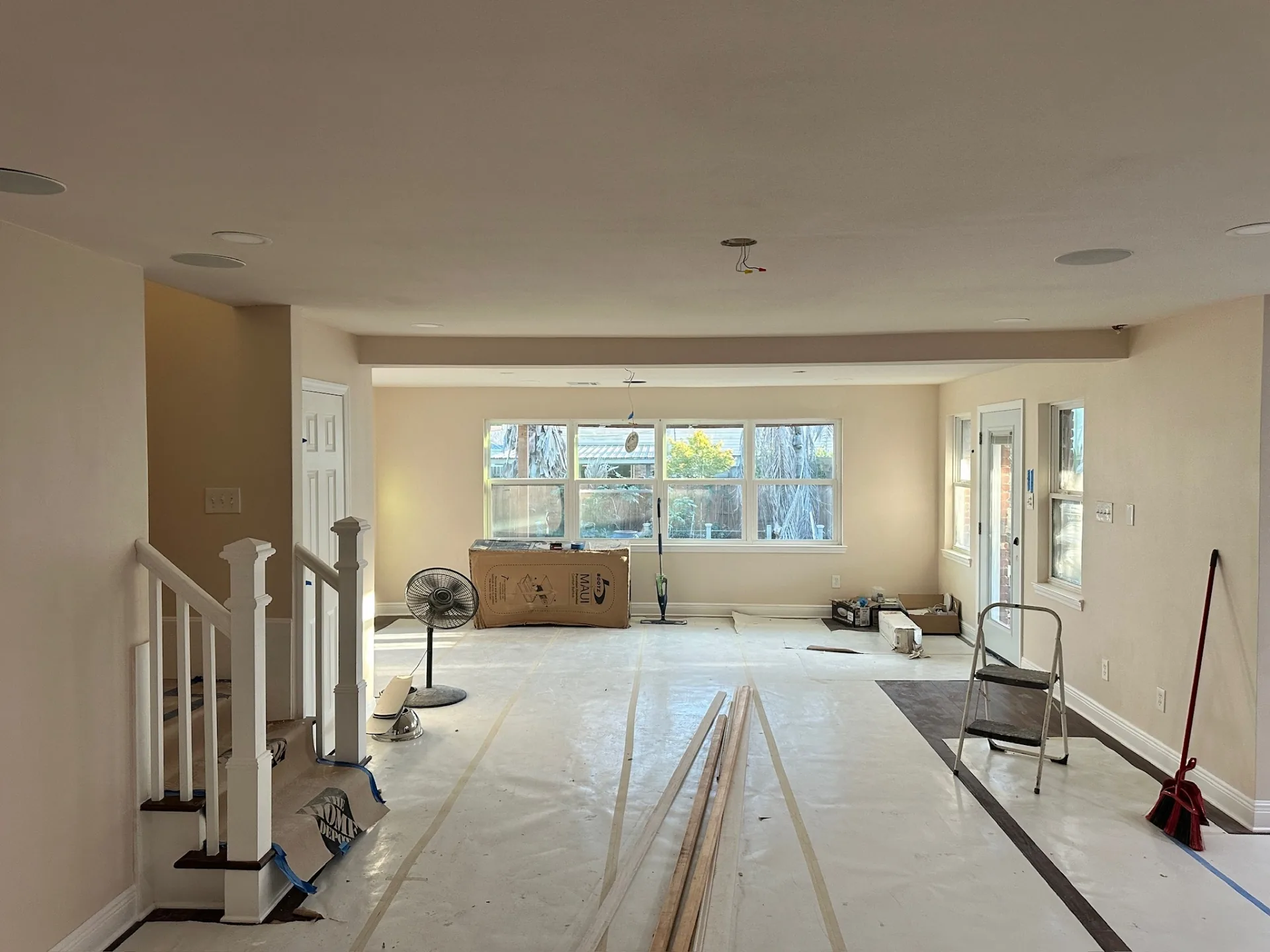 Open living and dining area at Blanke Street Metairie home post-paint with clean walls, ceiling speakers, recessed cans, and papered floor before final trim
