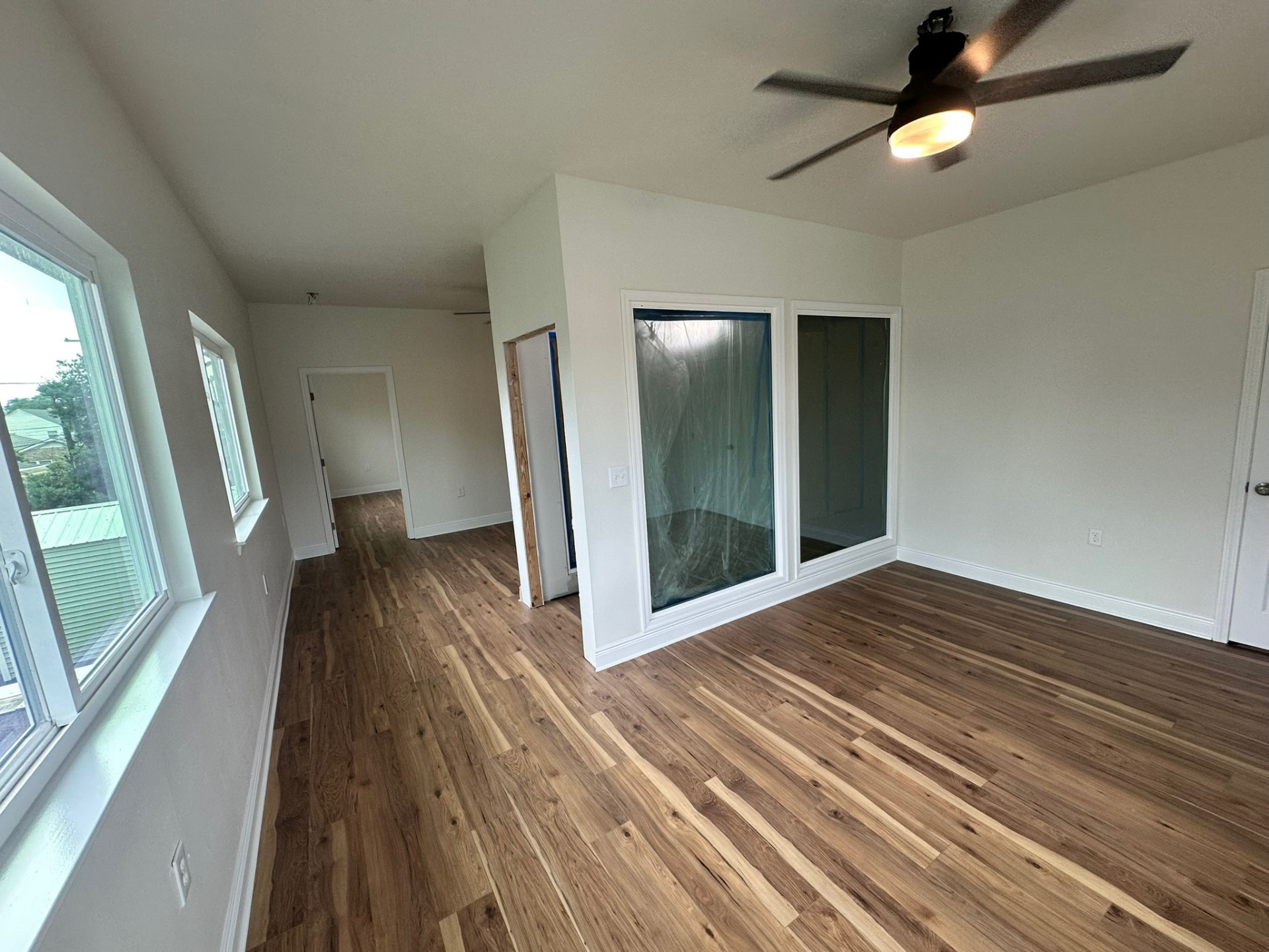 Finished second-floor loft and bedroom hallway on the Metairie addition with wide-plank wood-look flooring throughout, glass slider to the bedroom suite, casement windows along the side wall and ceiling fan with light