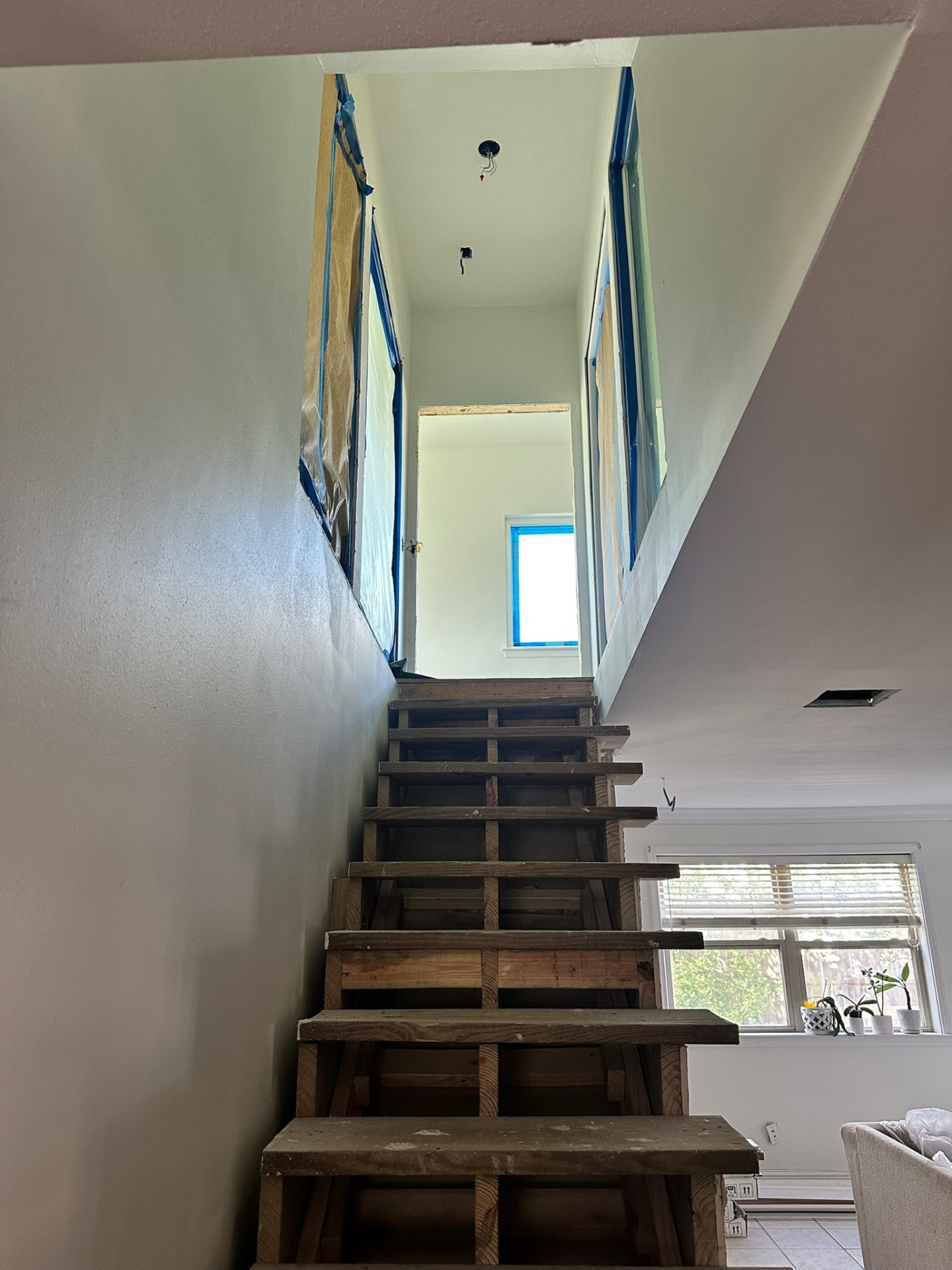 Open stair stringers leading up to vaulted second-floor landing in Metairie addition with stairwell walls masked in plastic and paper for paint prep