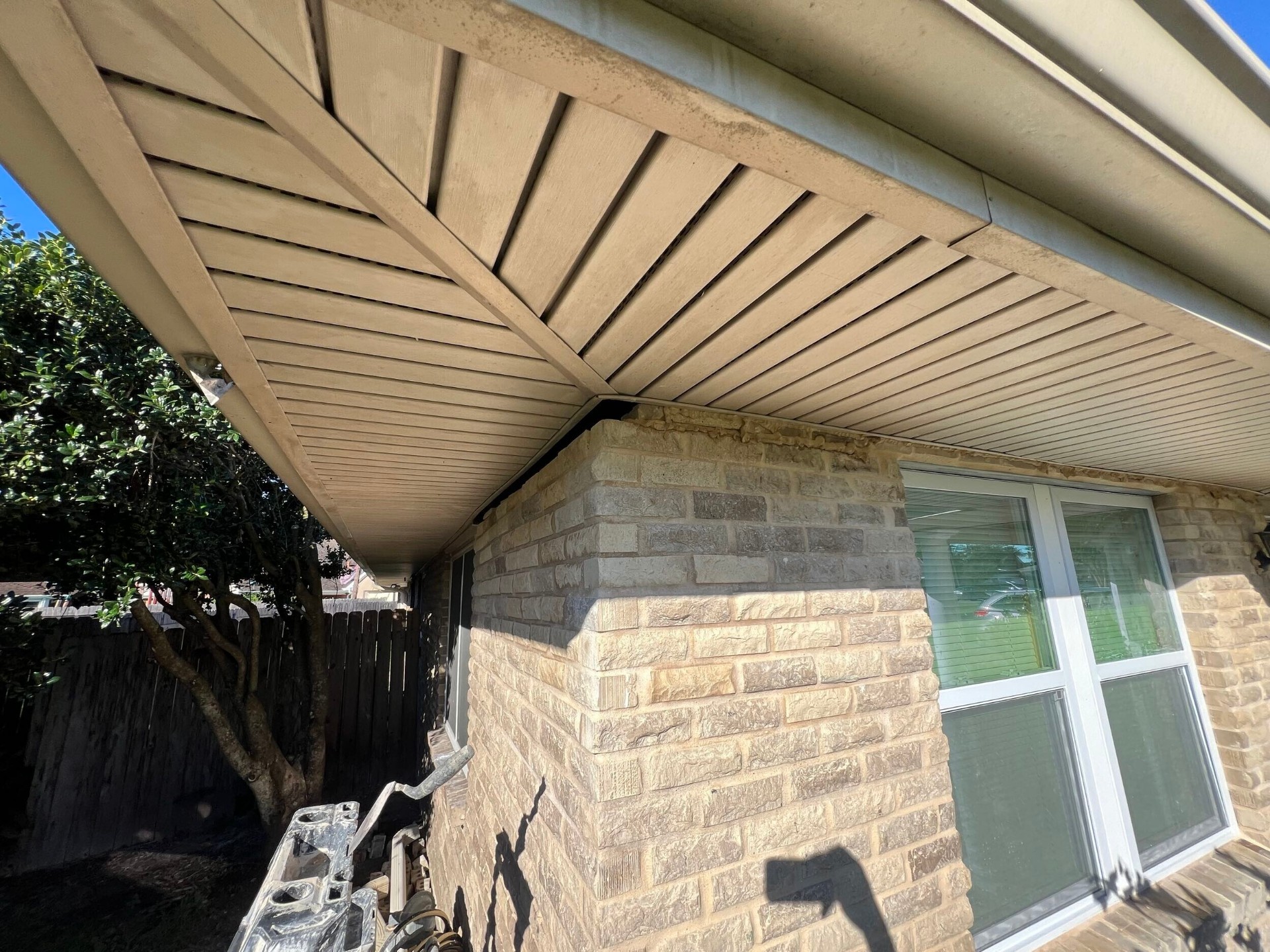 Exterior corner detail of the rebuilt Gretna home showing the T1-11 porch gable soffit, aluminum gutter, and rebuilt stone-look brick veneer column tie-in