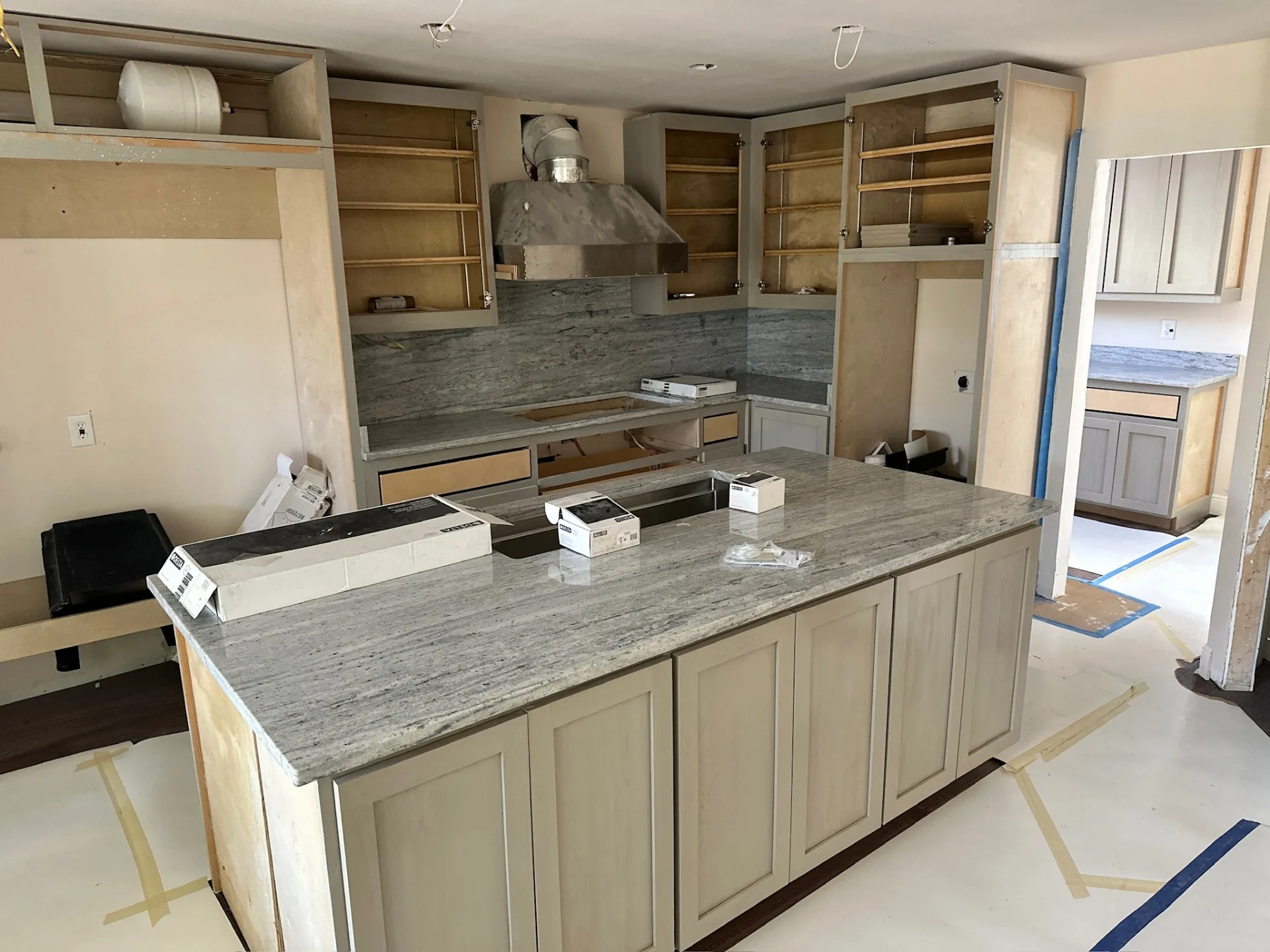 Kitchen at Blanke Street Metairie home mid-install with new granite countertops set, gray-stained shaker cabinets, stainless hood, and marble backsplash going up