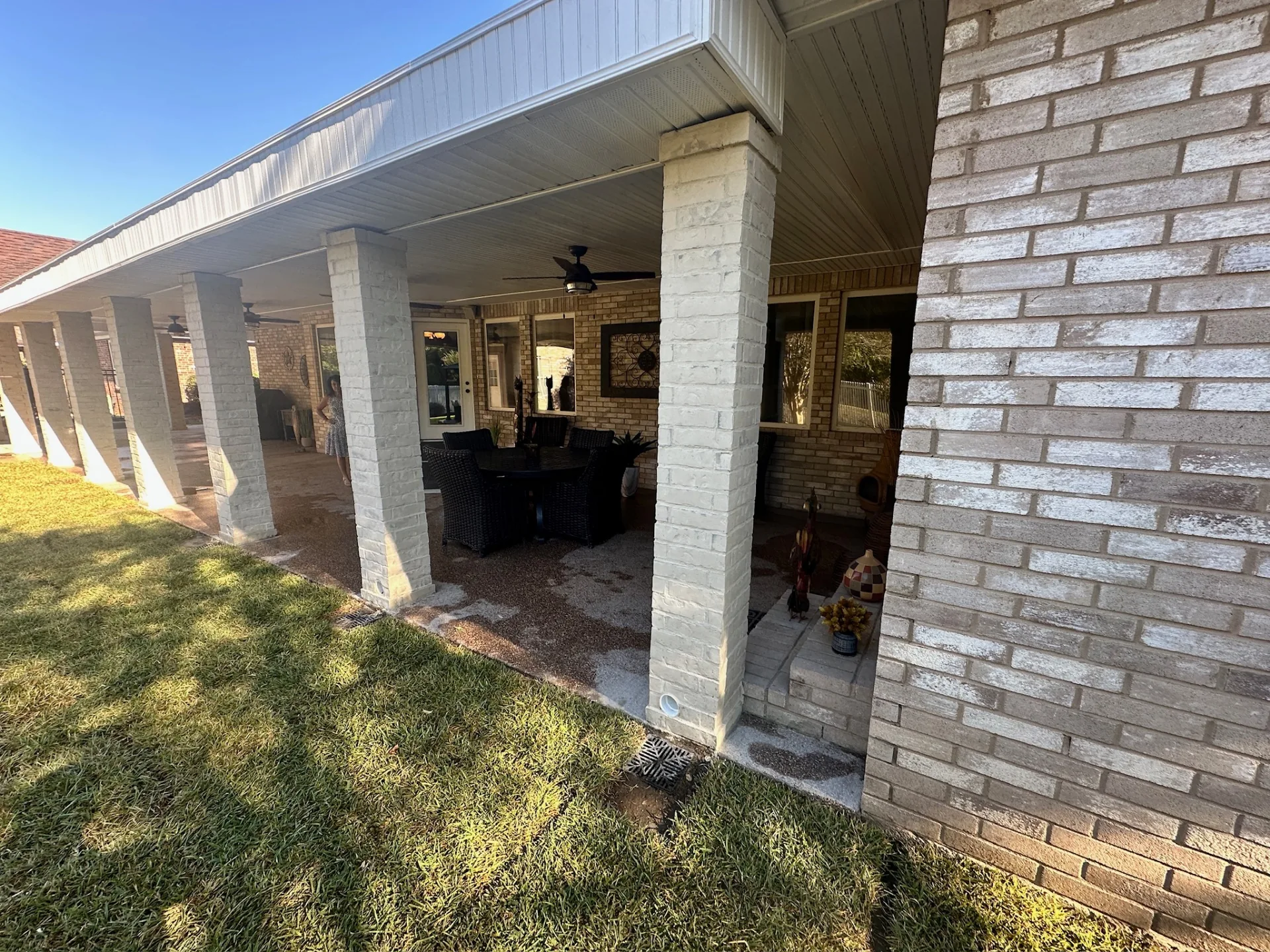 Finished rebuilt covered patio wrapping the rear of Destrehan Louisiana brick home with limewashed brick posts, matching shingle roof, and hidden gutters by Cajun Home Services