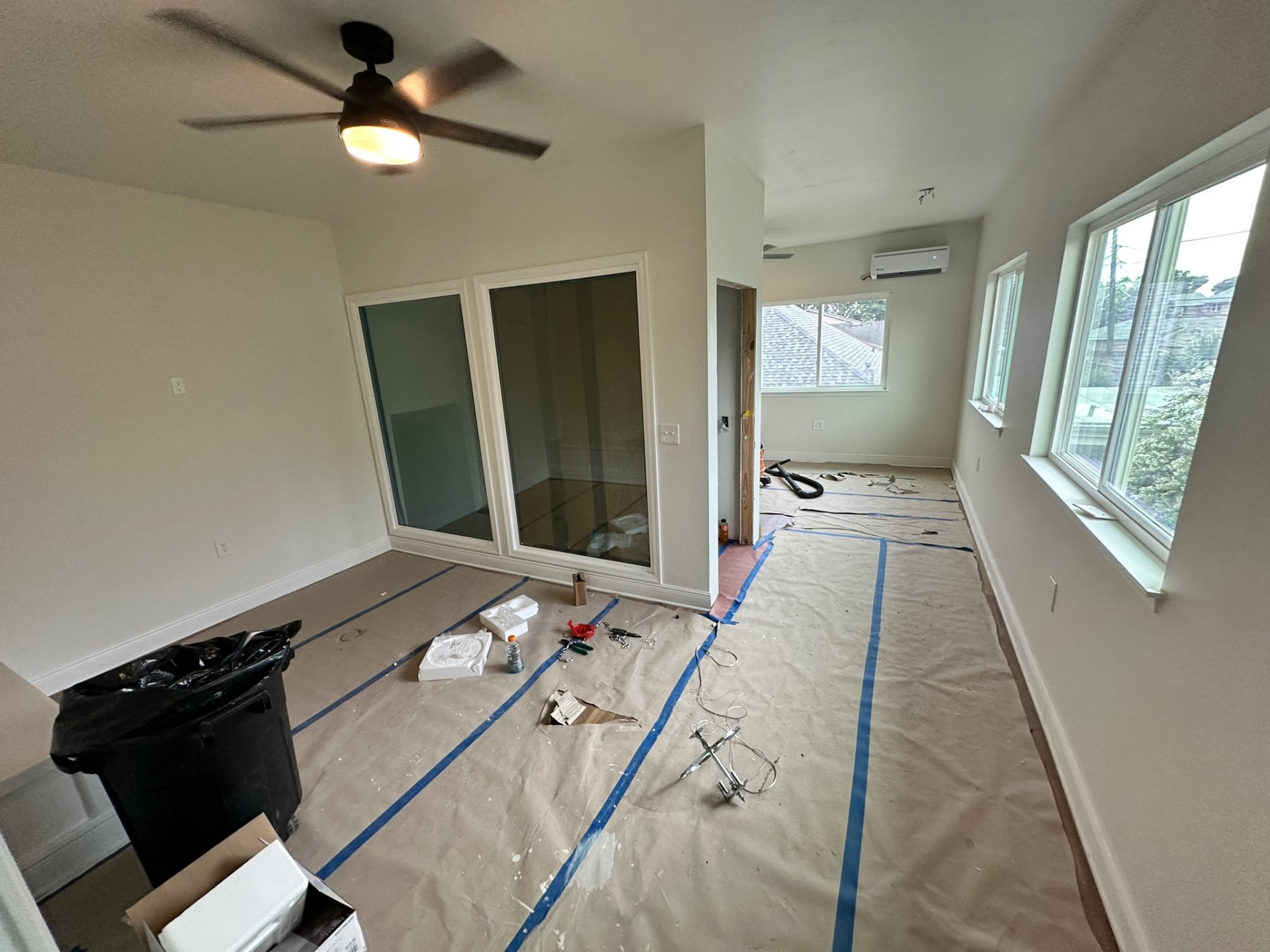 Finished second-floor loft on the Metairie addition with new interior glass slider doors to the master suite, large ceiling fan, wall of windows looking over the neighbors, ductless mini-split high on the rear wall and clean white walls during punch-out