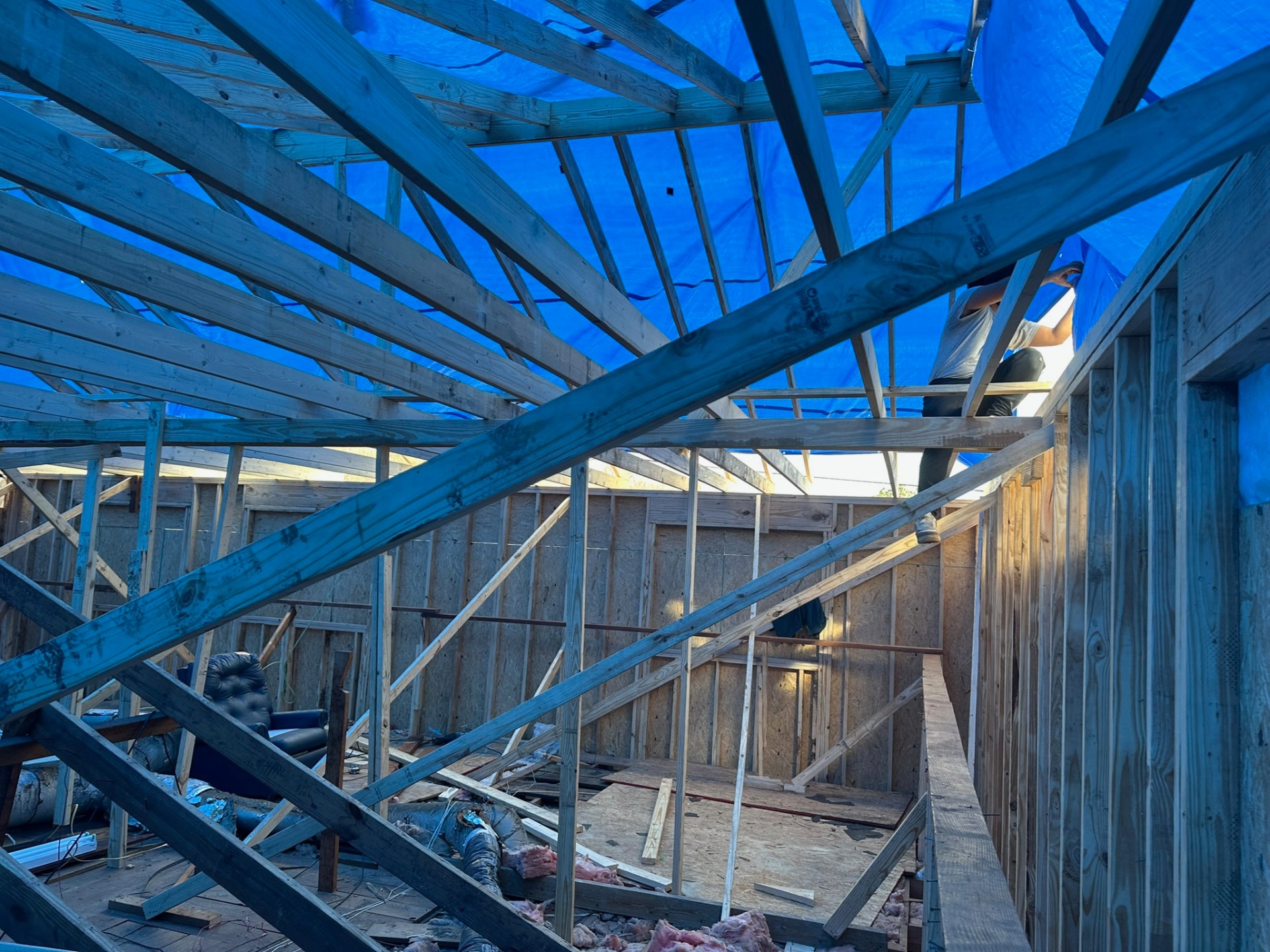 Carpenter working on new rafter framing inside Metairie attic with blue tarp suspended overhead to keep the interior dry during second-floor tear-off