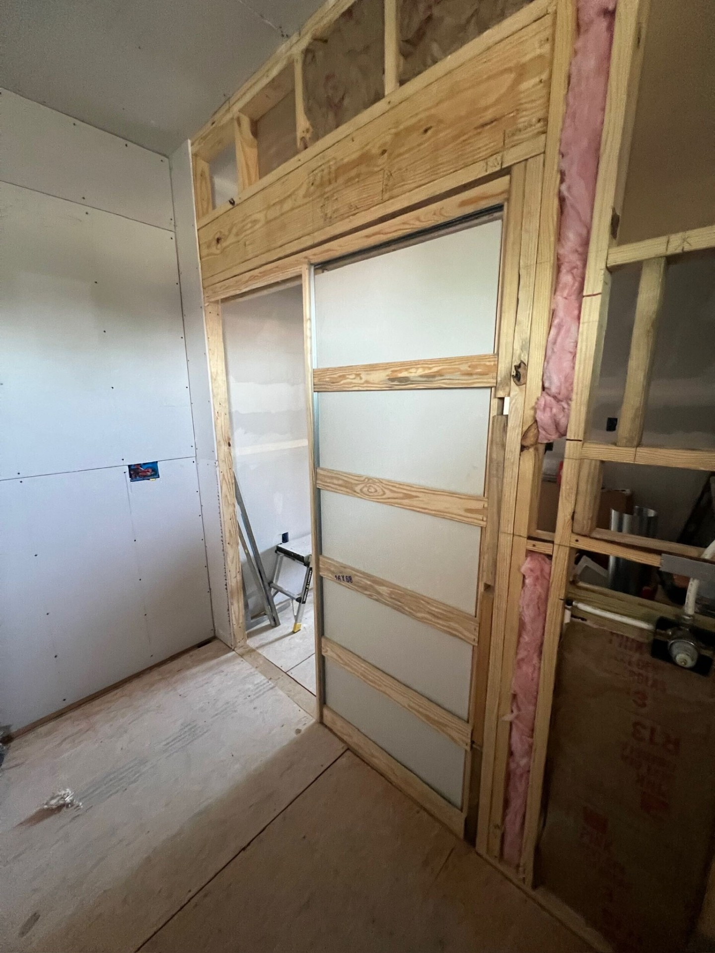 Interior of Metairie second-floor addition with rough-framed pocket door installed in new partition wall, drywall hung on adjacent wall and pink R-13 insulation visible in the open stud bay