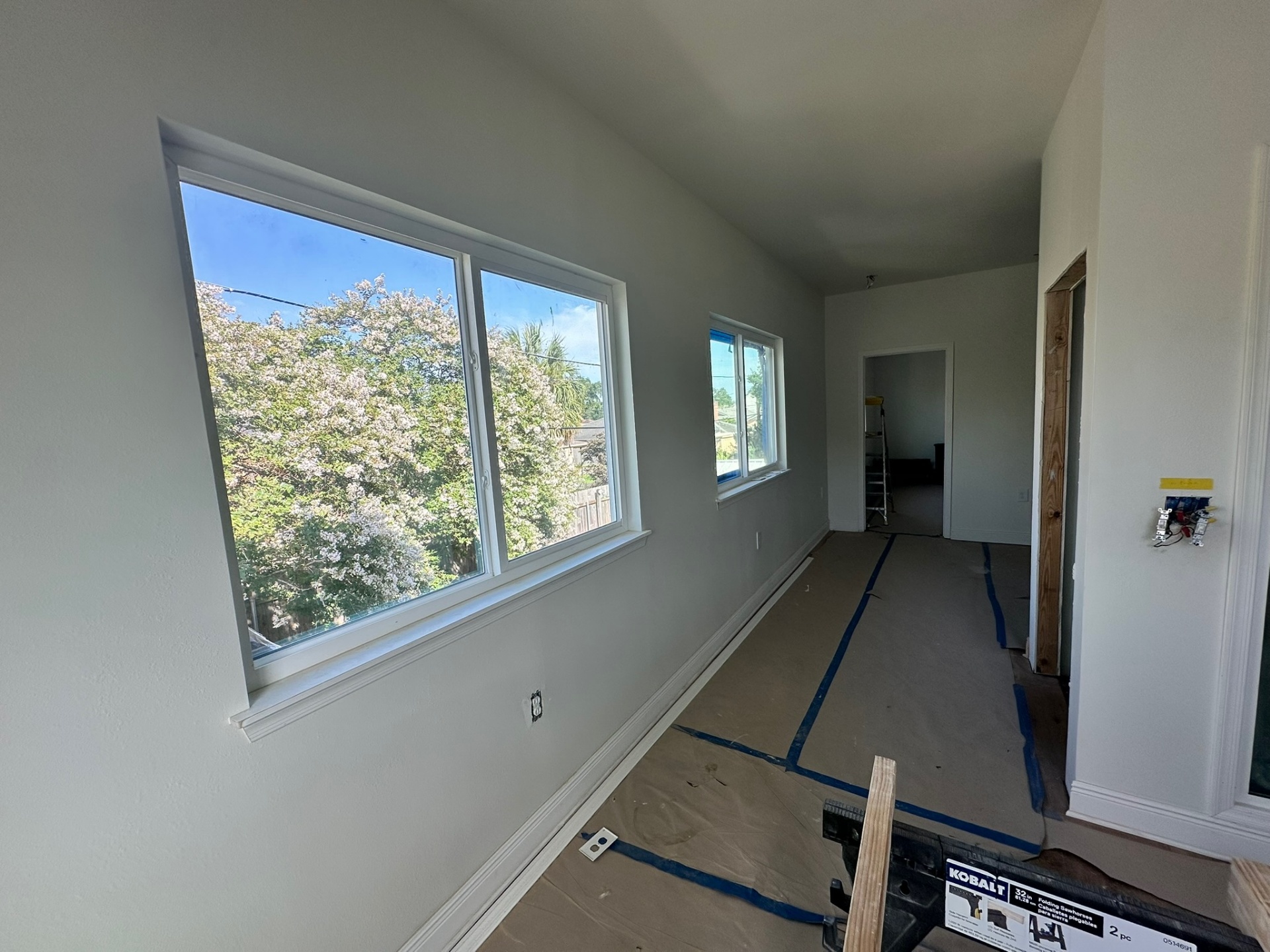 Second-floor hallway in Metairie addition with two double-hung windows, finished casing and baseboard, paint masked at switches, drop cloth on floor mid-paint