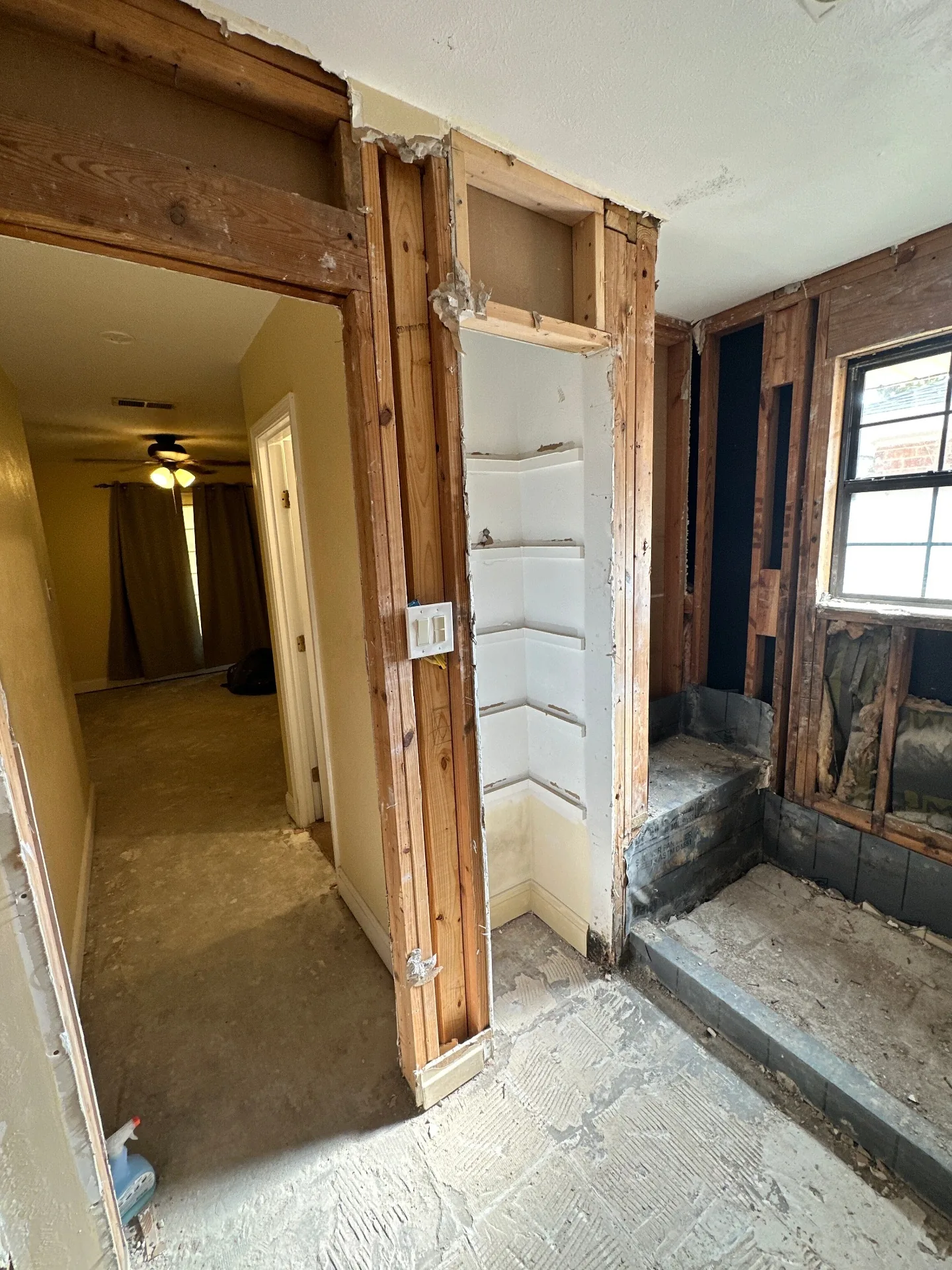 Interior demo view at Blanke Street Metairie home with hallway bath walls opened to studs, tile shower pan exposed, and framing visible around the doorway