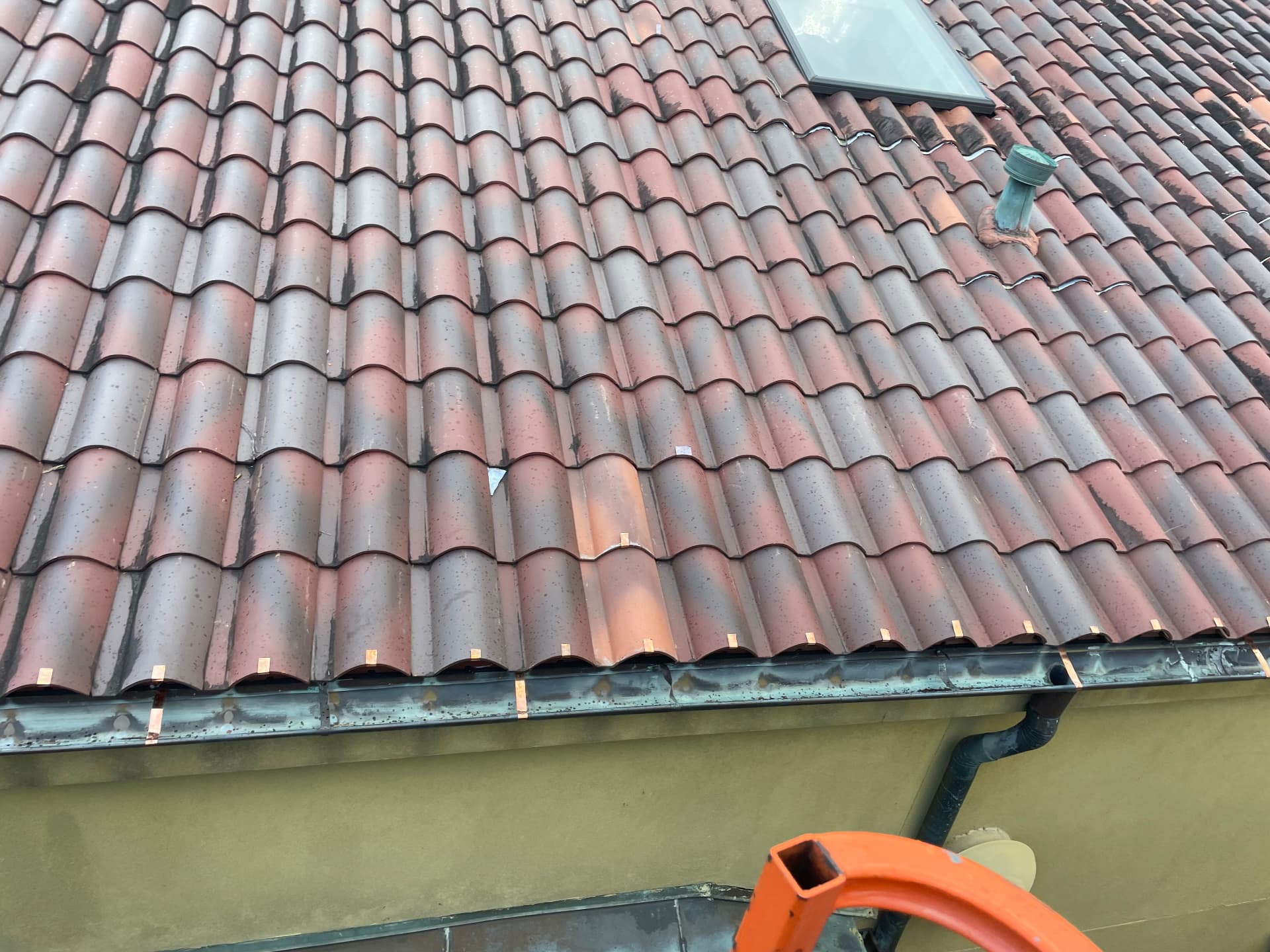 Repaired terra cotta tile roof field with replacement tiles blended in near a skylight in Metairie Louisiana