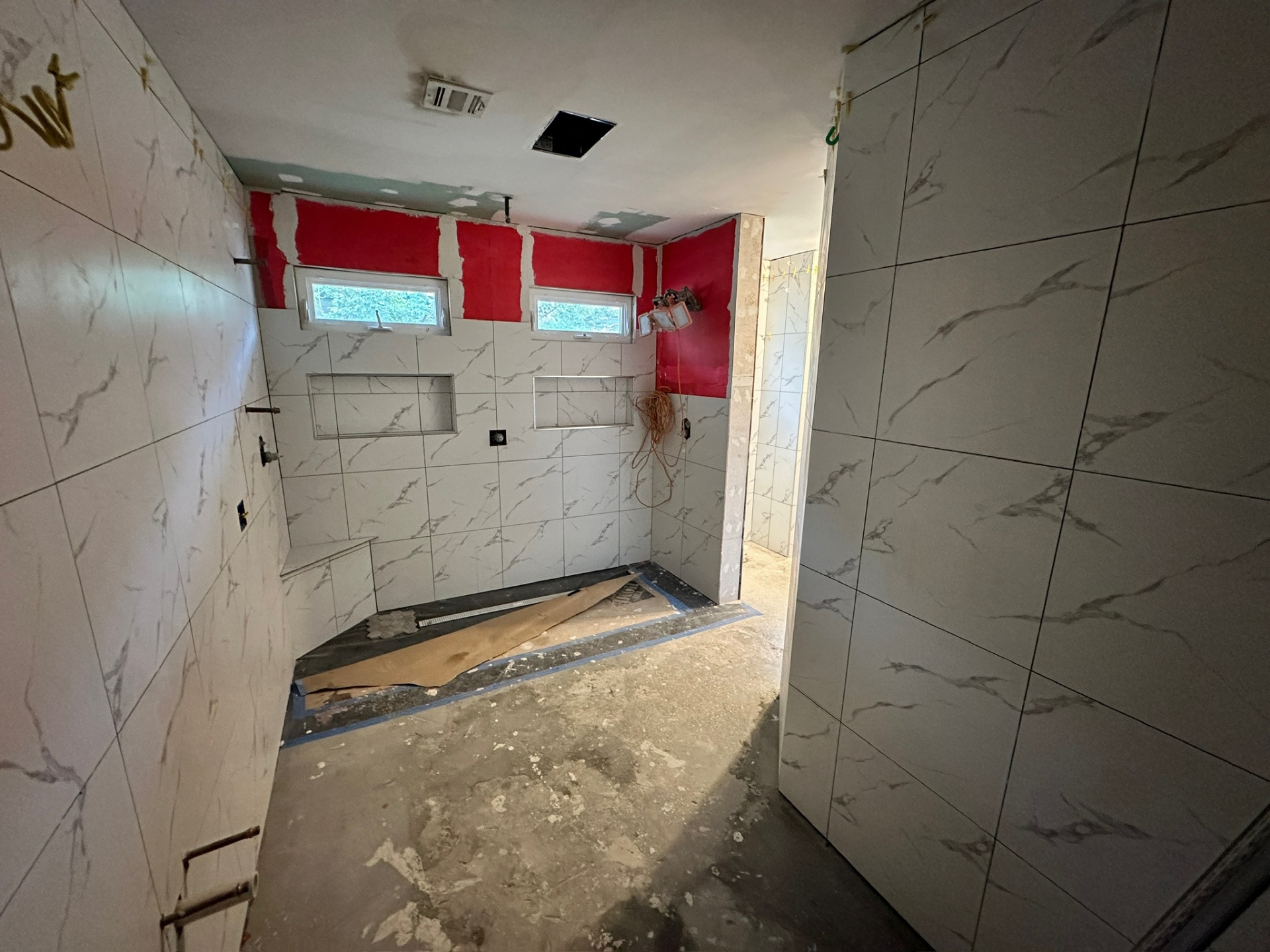 Shower fully tiled with a red RedGard band above the awning windows before the ceiling and floor go in at Metairie master bath