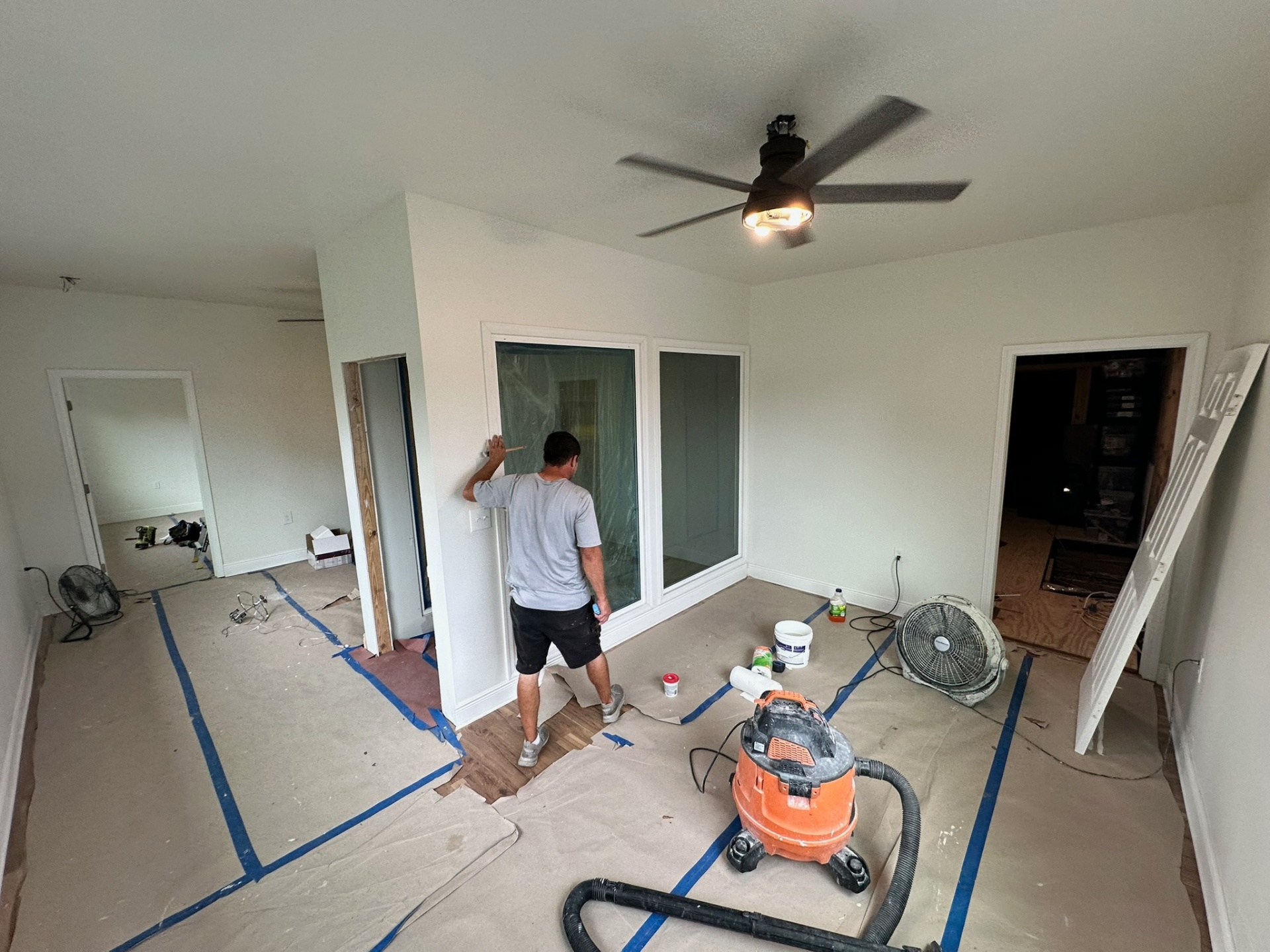 Cajun Home Services installer marking the wall next to a new interior glass slider on the second floor of the Metairie addition, with floor protection, ceiling fan, shop vac, fans and lumber staged for finish work