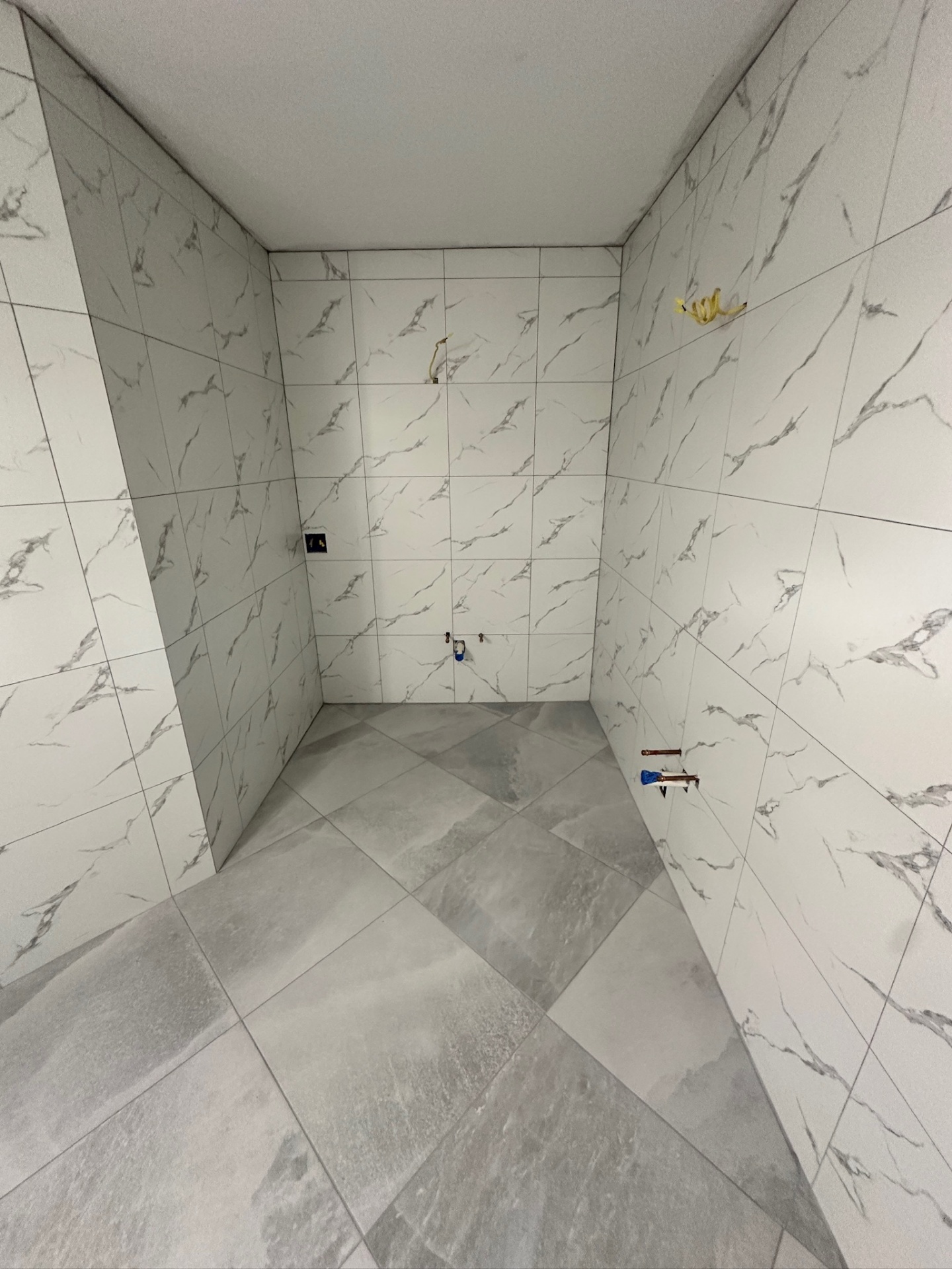 Water closet alcove with marble-look walls and gray porcelain floor tile complete in Metairie master bath