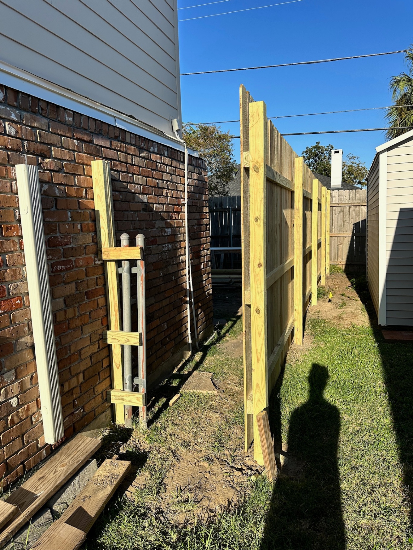 View down the side yard of the Metairie second-floor addition showing new treated fence framing against the existing brick wall with plumb posts and horizontal rails