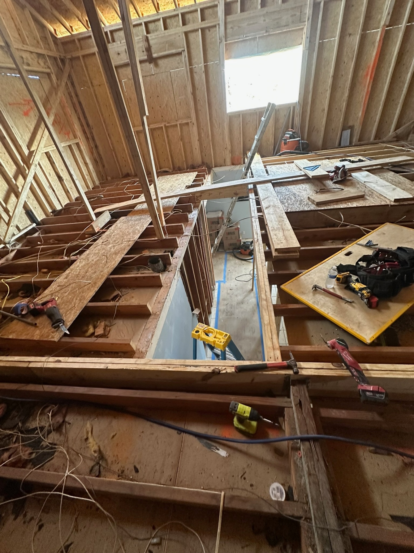 Framed stairwell opening cut through new second-floor joists inside Metairie addition with tools and lumber staged around the opening