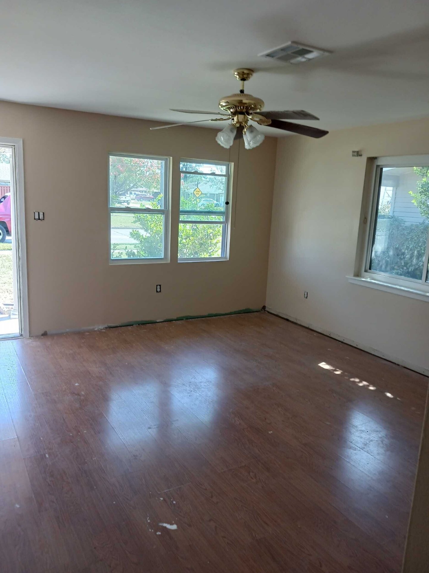 Wide interior view of the rebuilt Gretna living room with primed walls, new windows on two exposures, and ceiling fan ready for final paint