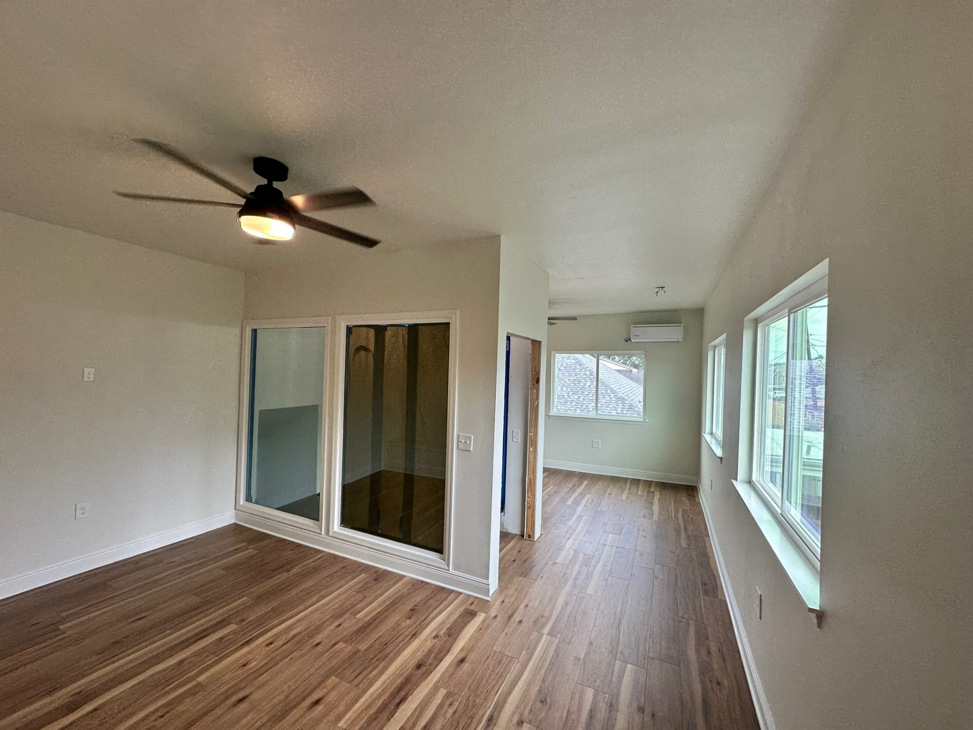 Wide view of the finished second-floor loft living area on the Metairie addition with engineered wood flooring, dual glass sliders to the new master bedroom, large rear window, ductless mini-split and bronze ceiling fan with light