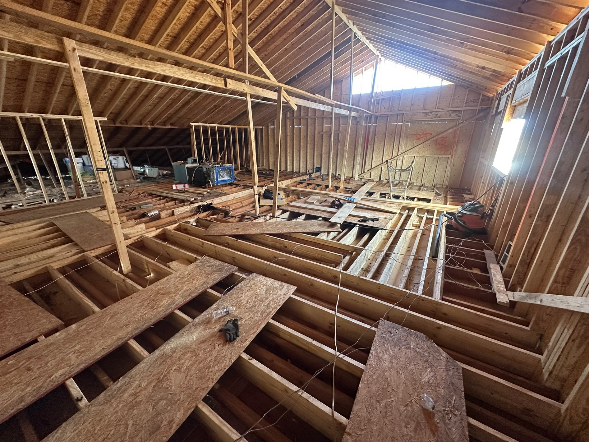 Vaulted interior of new Metairie second-floor framing with rafters fanning out to the ridge, sunlight through a gable vent and OSB walking boards across the floor joists
