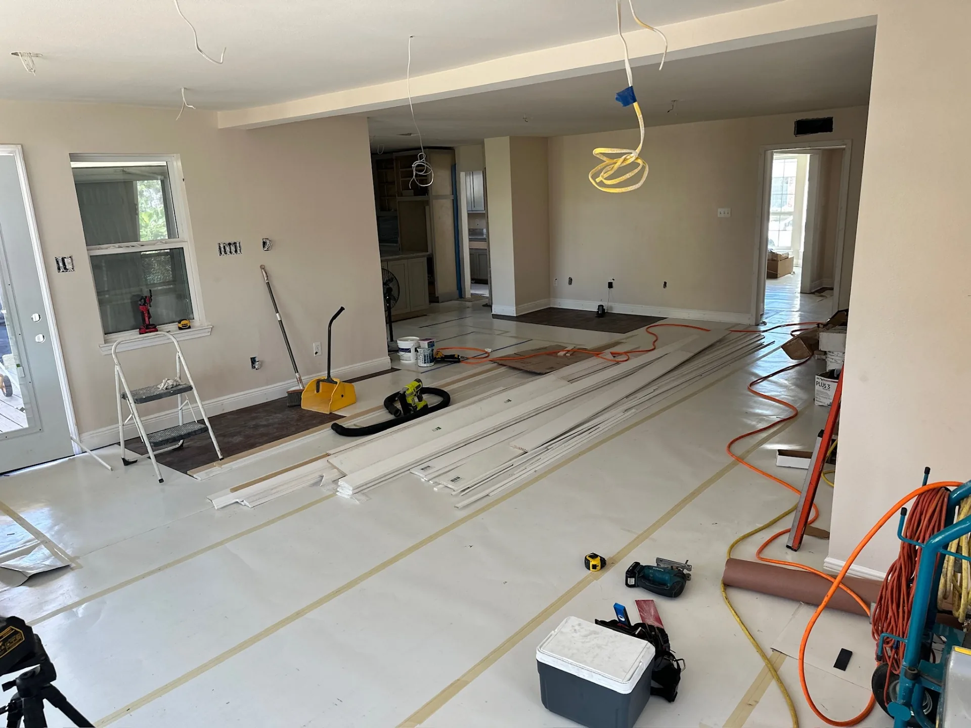 Open living and dining area at Blanke Street Metairie home mid-remodel with rosin paper on the floor, trim stock staged, and new laminate flooring being started near the rear door