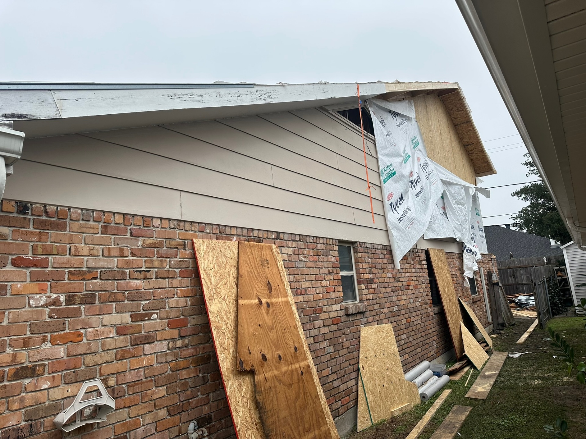 Close-up of Metairie home showing original first-floor siding with new second-floor sheathing and Tyvek wrap rising directly above it