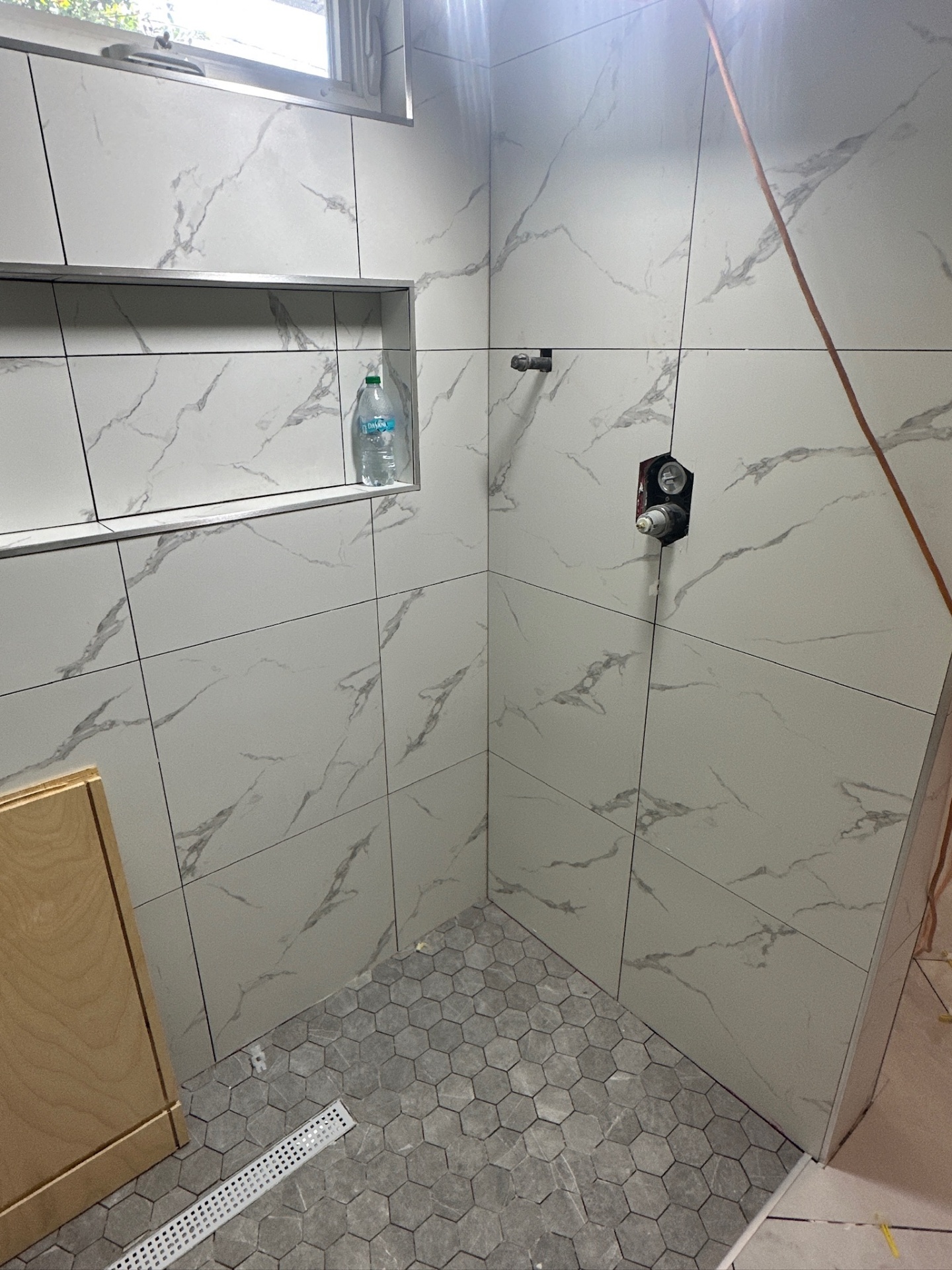 Shower corner with tiled niche, valve, and hex mosaic floor with linear drain in Metairie master bath
