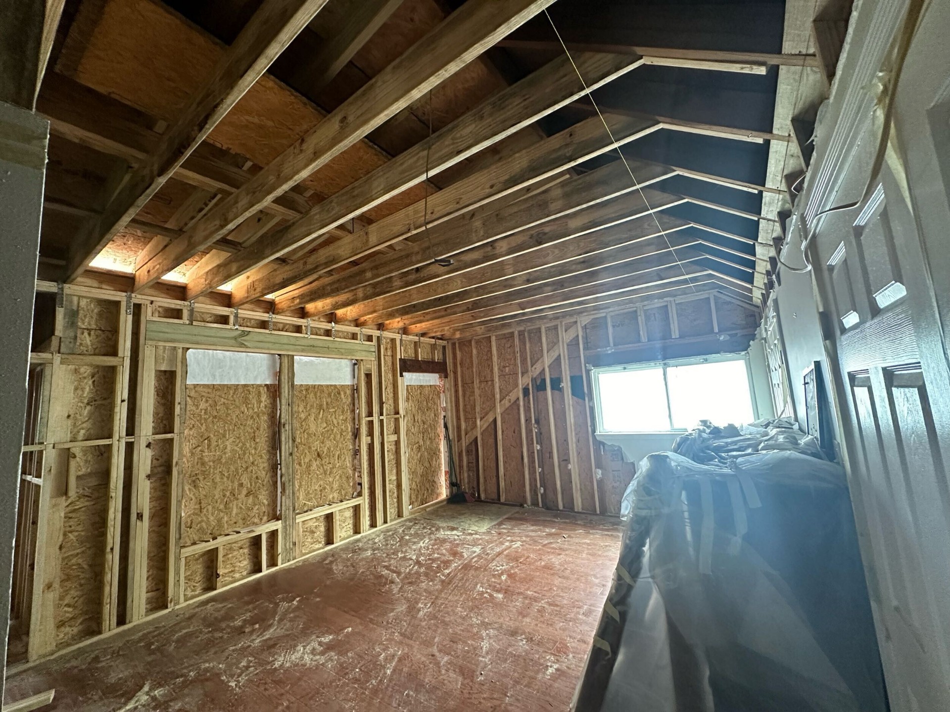 Second-story interior with new ceiling rafters, sheathed walls, and rough window openings at Blanke Street Metairie whole-home remodel