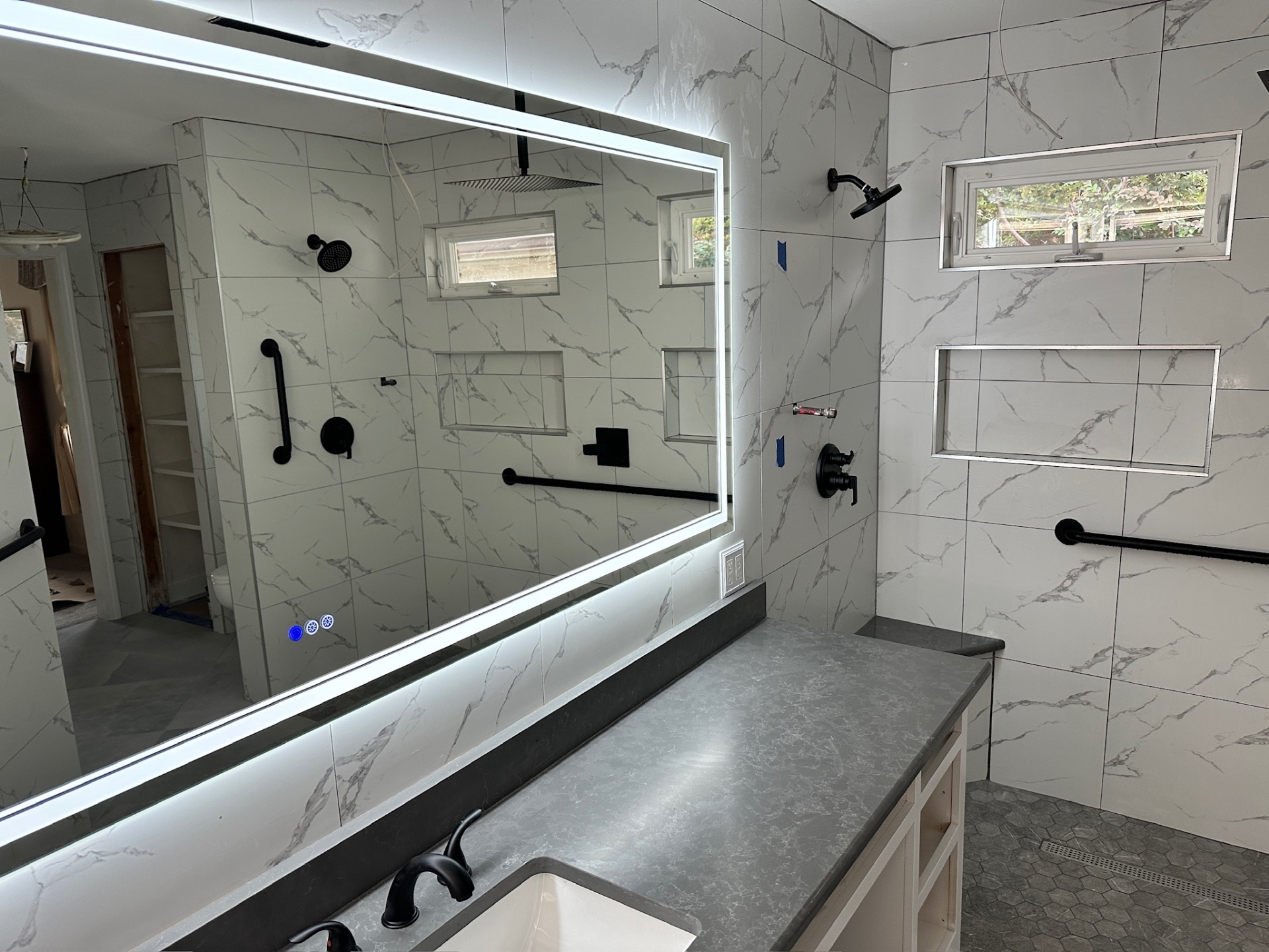 Wide LED-backlit vanity mirror reflecting the walk-in shower with dual heads and dual niches in Metairie master bath