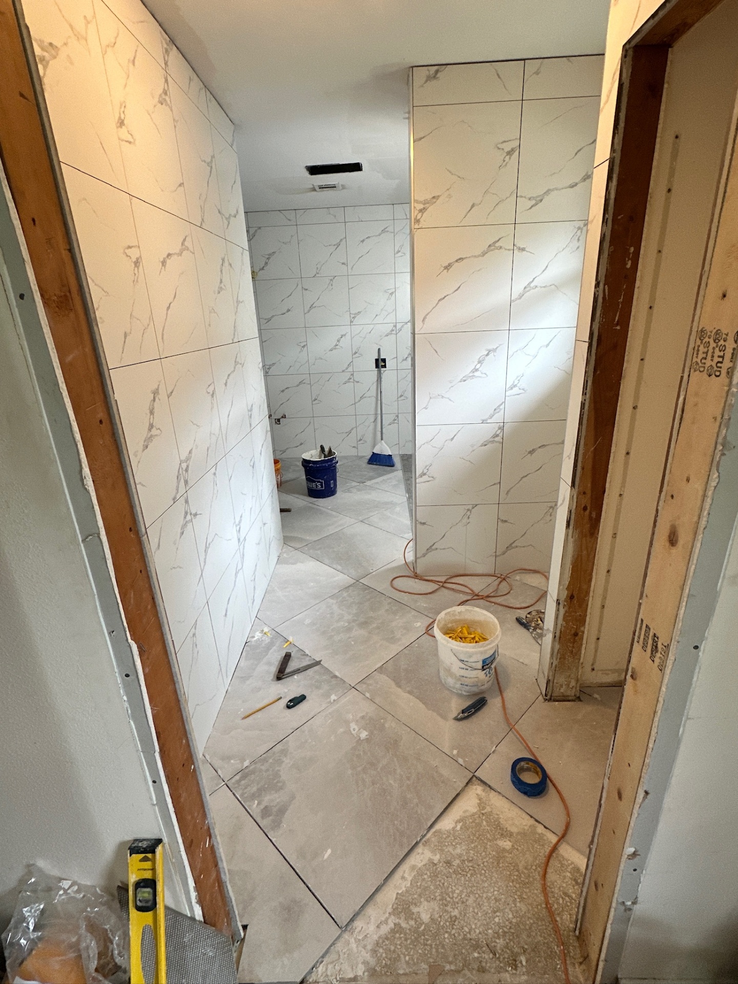 Marble-look wall tile and gray porcelain floor tile complete in the hallway of Metairie master bath