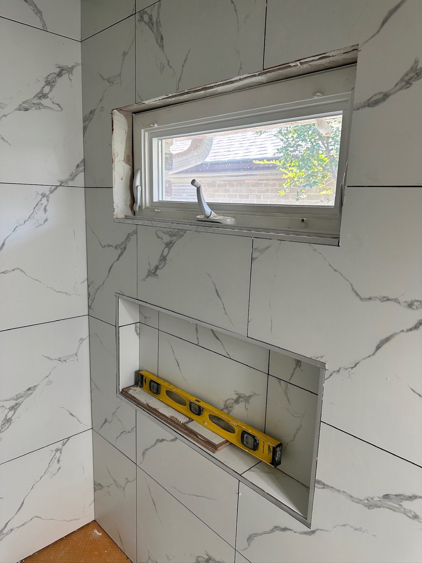 Level checked on freshly set shower niche shelf with Schluter edges under the awning window in Metairie master bath