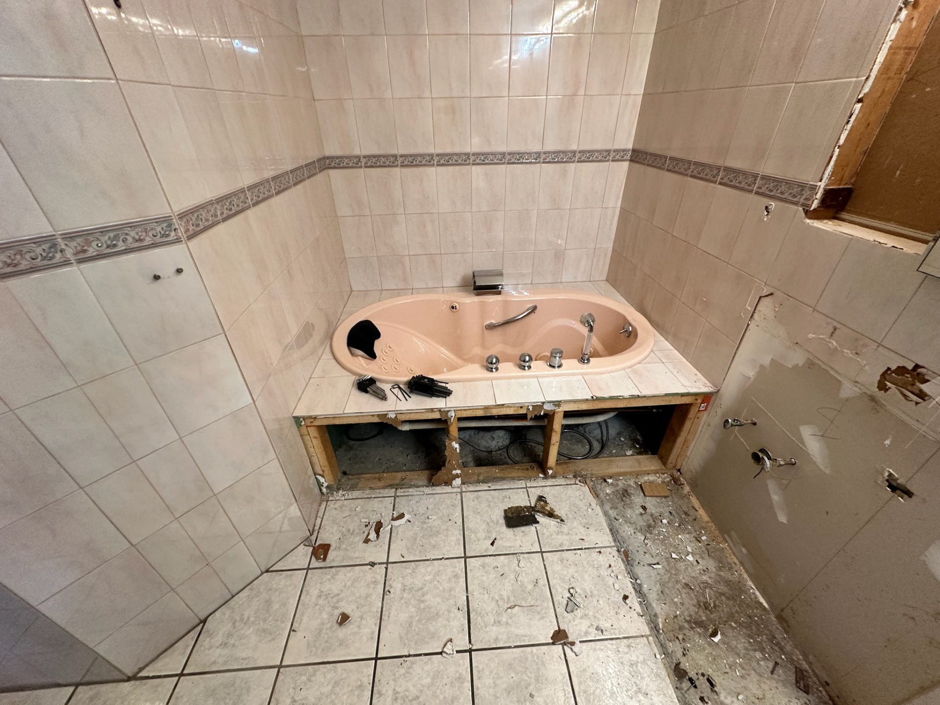 Peach jetted corner tub isolated with front tile panel removed during Metairie master bath demo