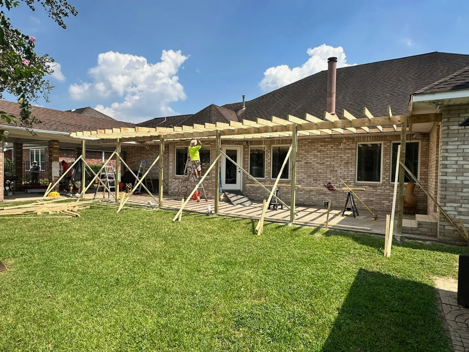 Wide yard view of new pergola-style pressure-treated rafter framing installed along Destrehan Louisiana home during covered patio replacement