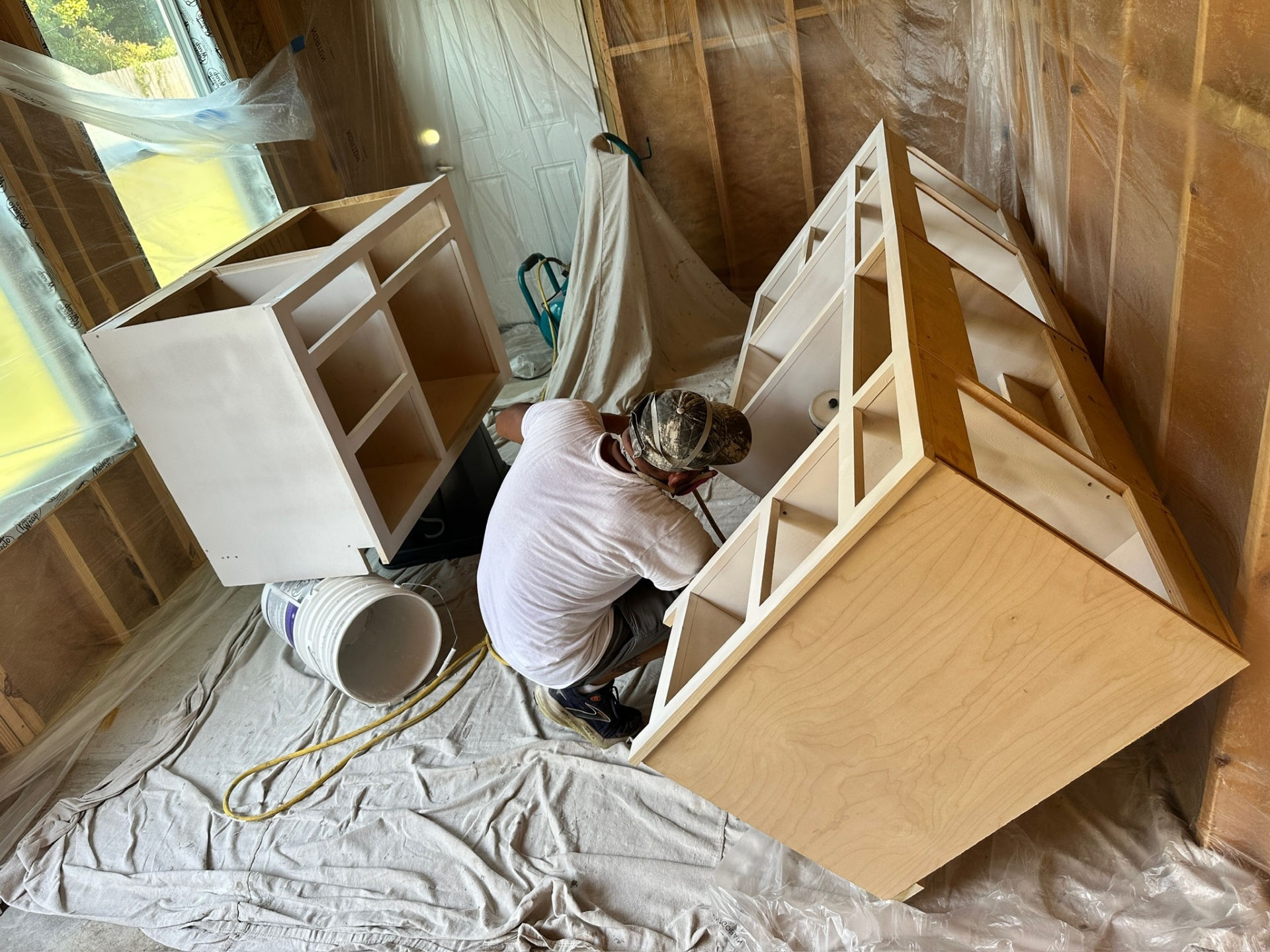 Custom vanity cabinet base boxes primed white inside a plastic-tented spray booth at the Metairie master bath project