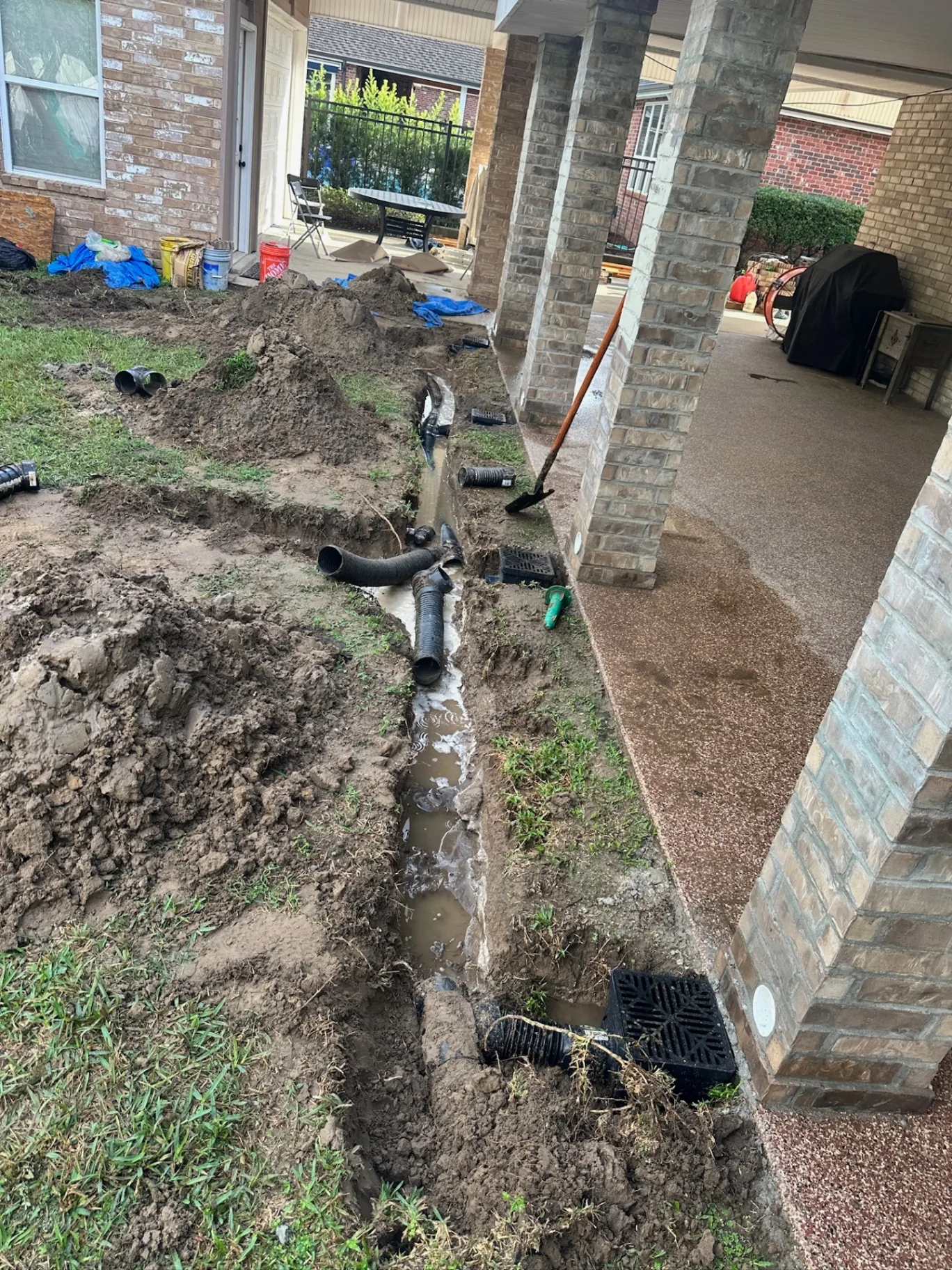 Detail view of drainage trench and corrugated pipe running between new brick-wrapped patio posts at Destrehan Louisiana home