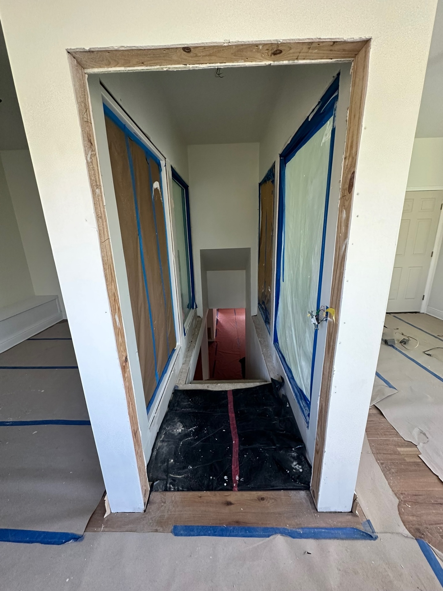 View looking down the second-floor stairwell from upstairs doorway with red rosin paper protecting treads, blue plastic on walls and finished engineered wood floor at landing