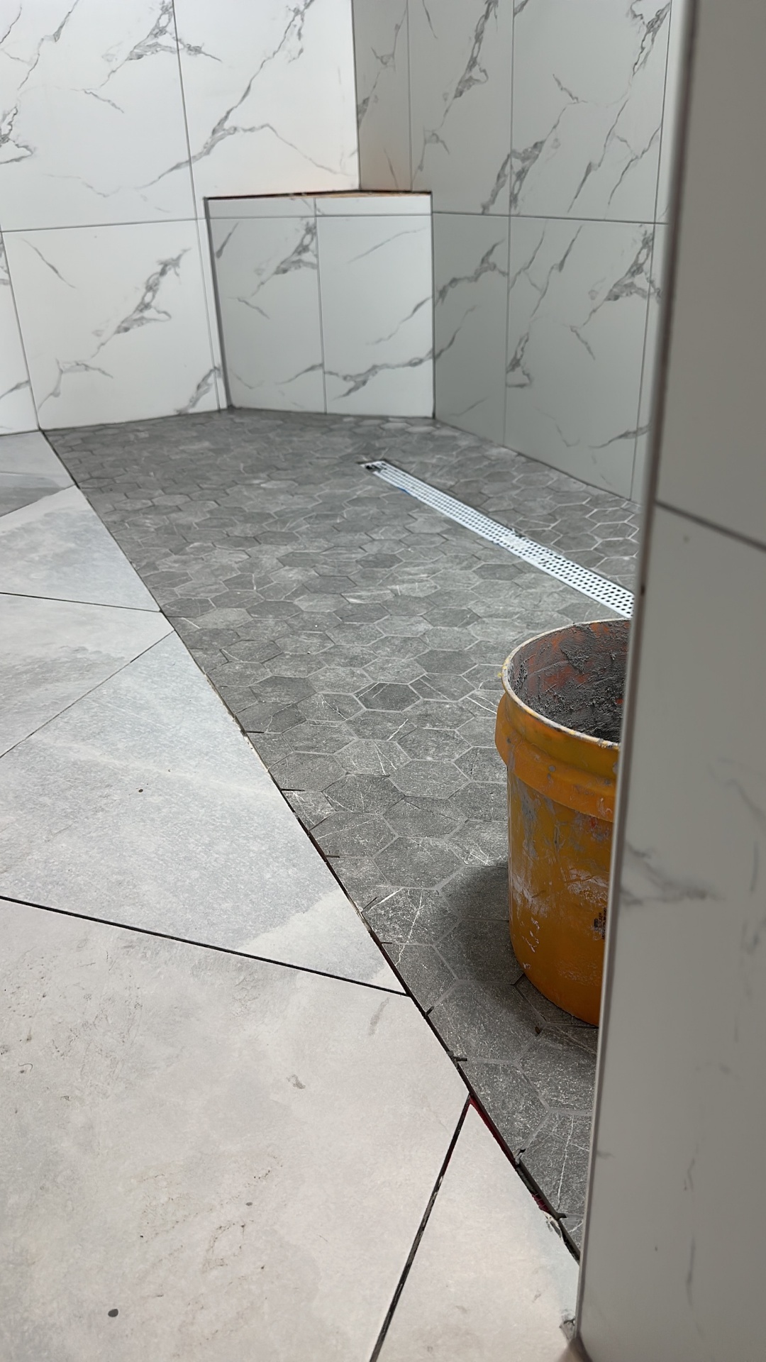 Gray hex mosaic shower floor with linear drain and marble-look walls in Metairie master bath