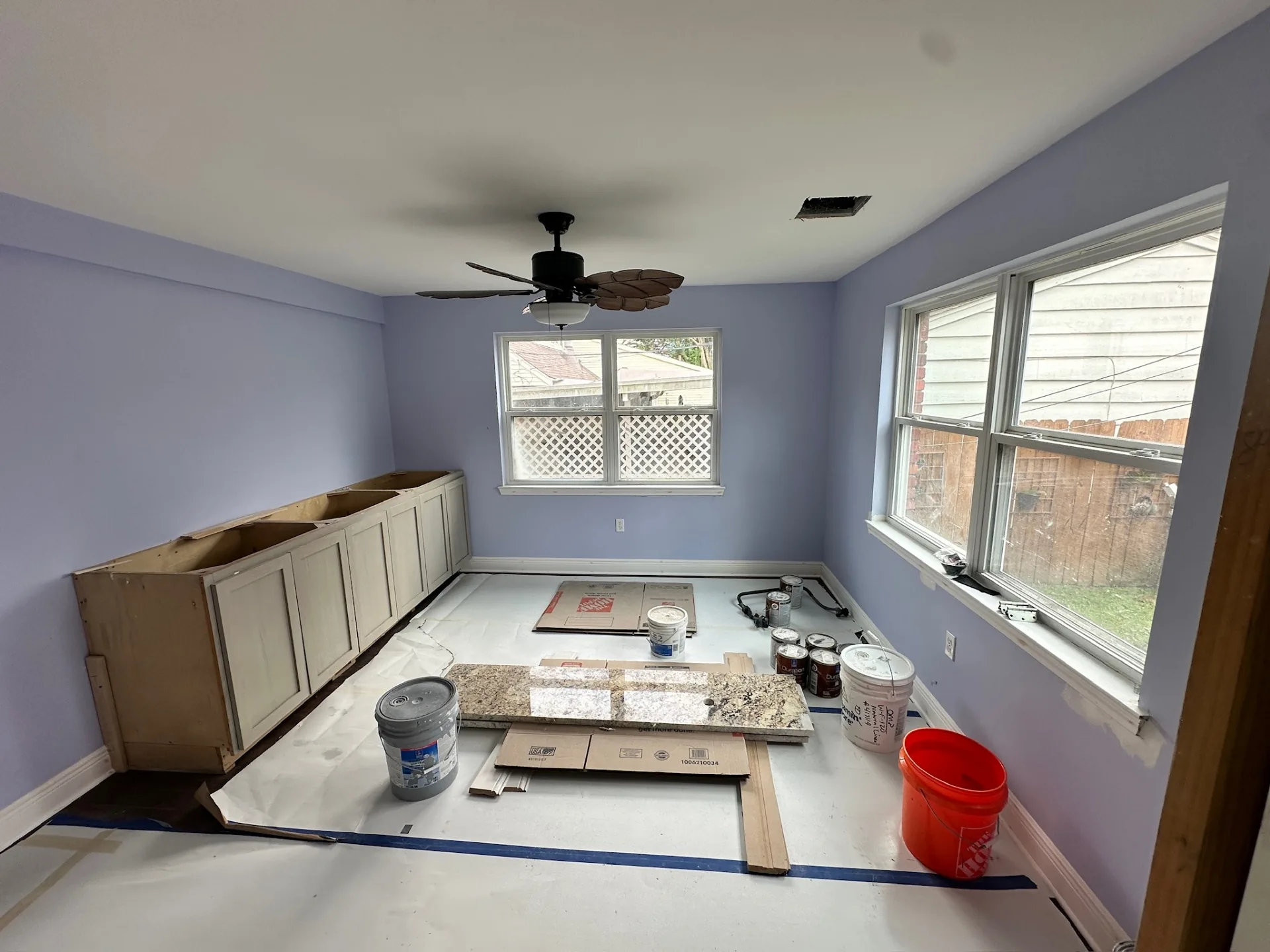 Interior bedroom at Blanke Street Metairie home mid-remodel with lavender walls, old built-in cabinet base, and a new granite slab staged on the floor with paint supplies