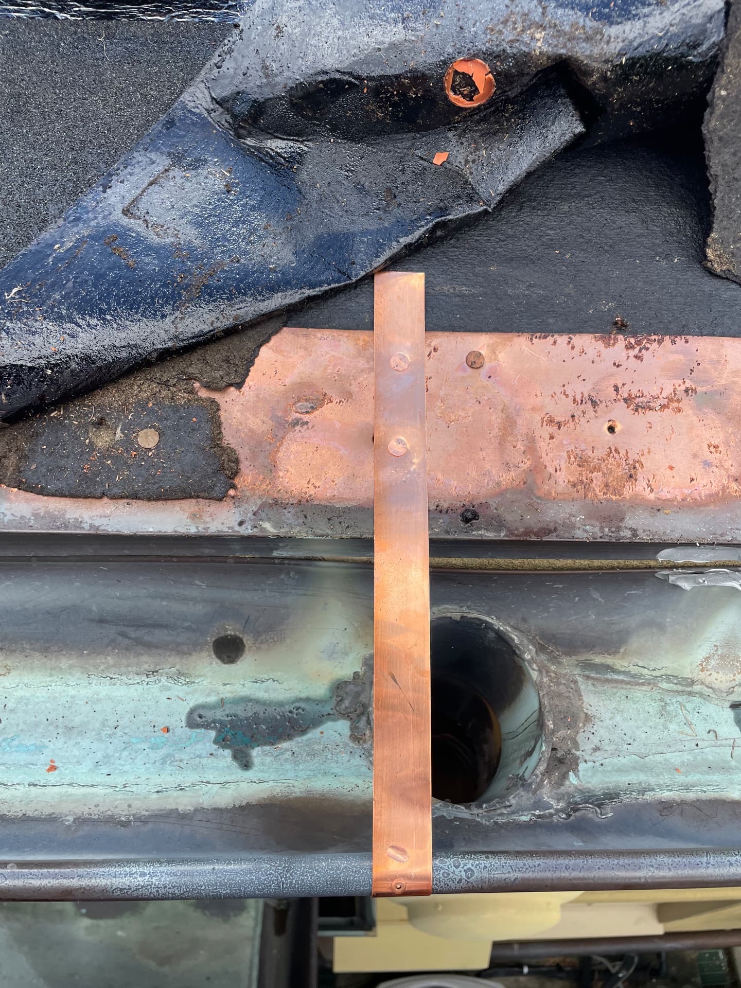 Close view of a new copper hanger strap and repaired downspout outlet in a half round copper gutter in Metairie Louisiana