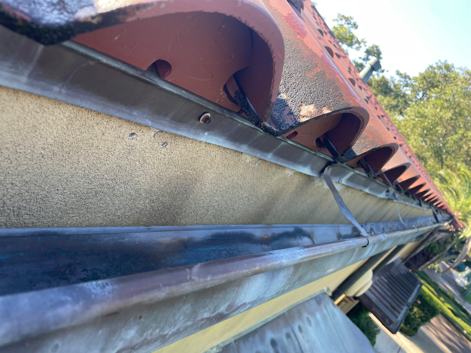 Underside view of a copper gutter separating from the fascia below terra cotta tiles in Metairie Louisiana