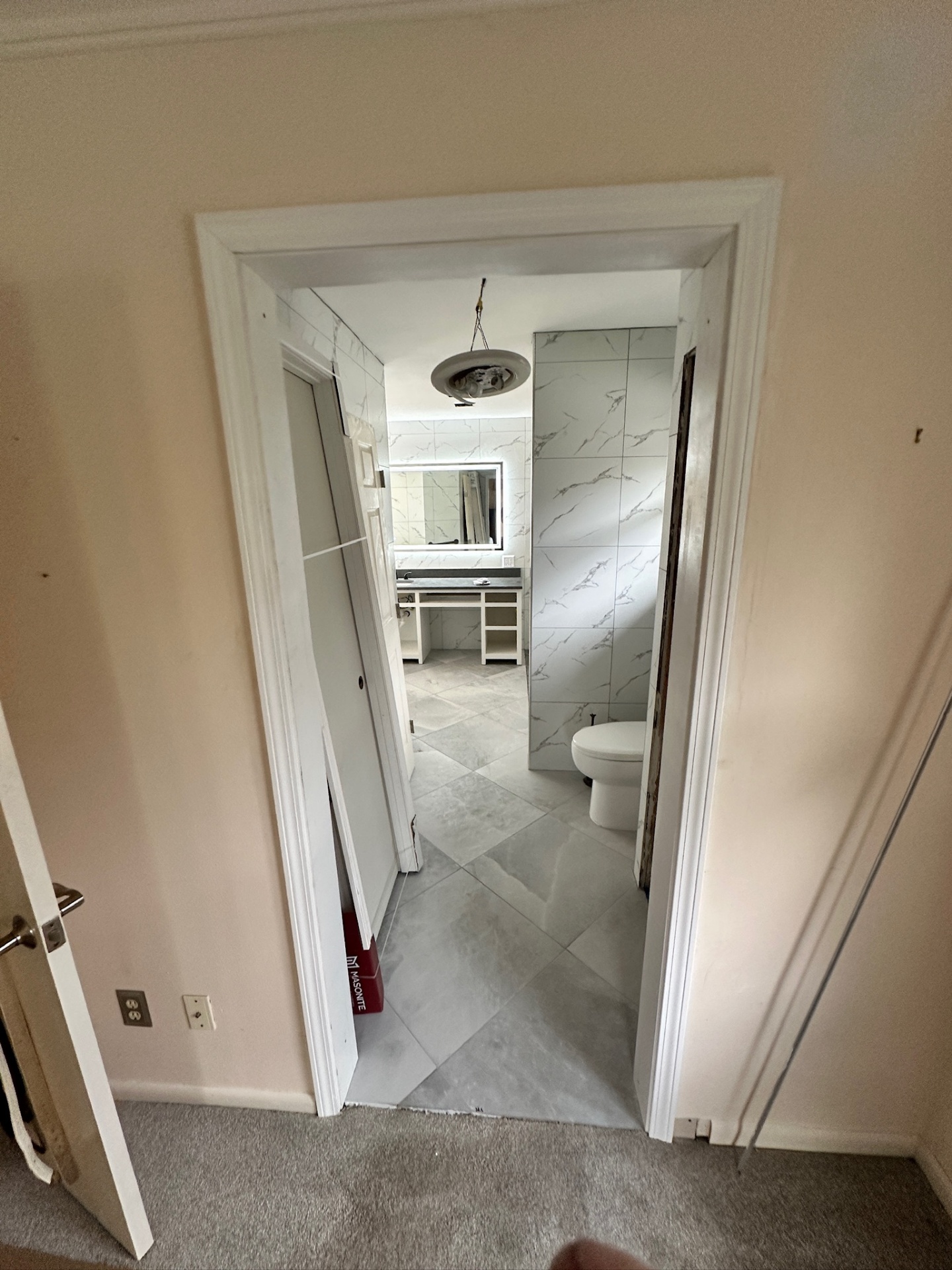 View from the bedroom doorway looking into the finished master bath with tiled walls, LED mirror, vanity, and toilet visible in Metairie