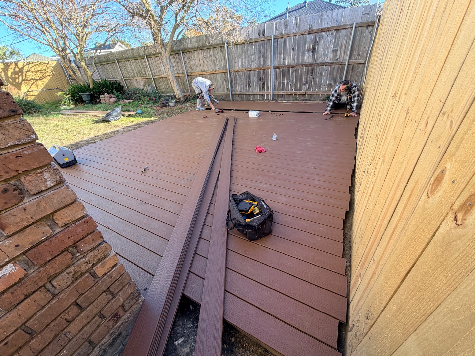 Two Cajun Home Services carpenters installing composite deck planks along back fence in Metairie Louisiana
