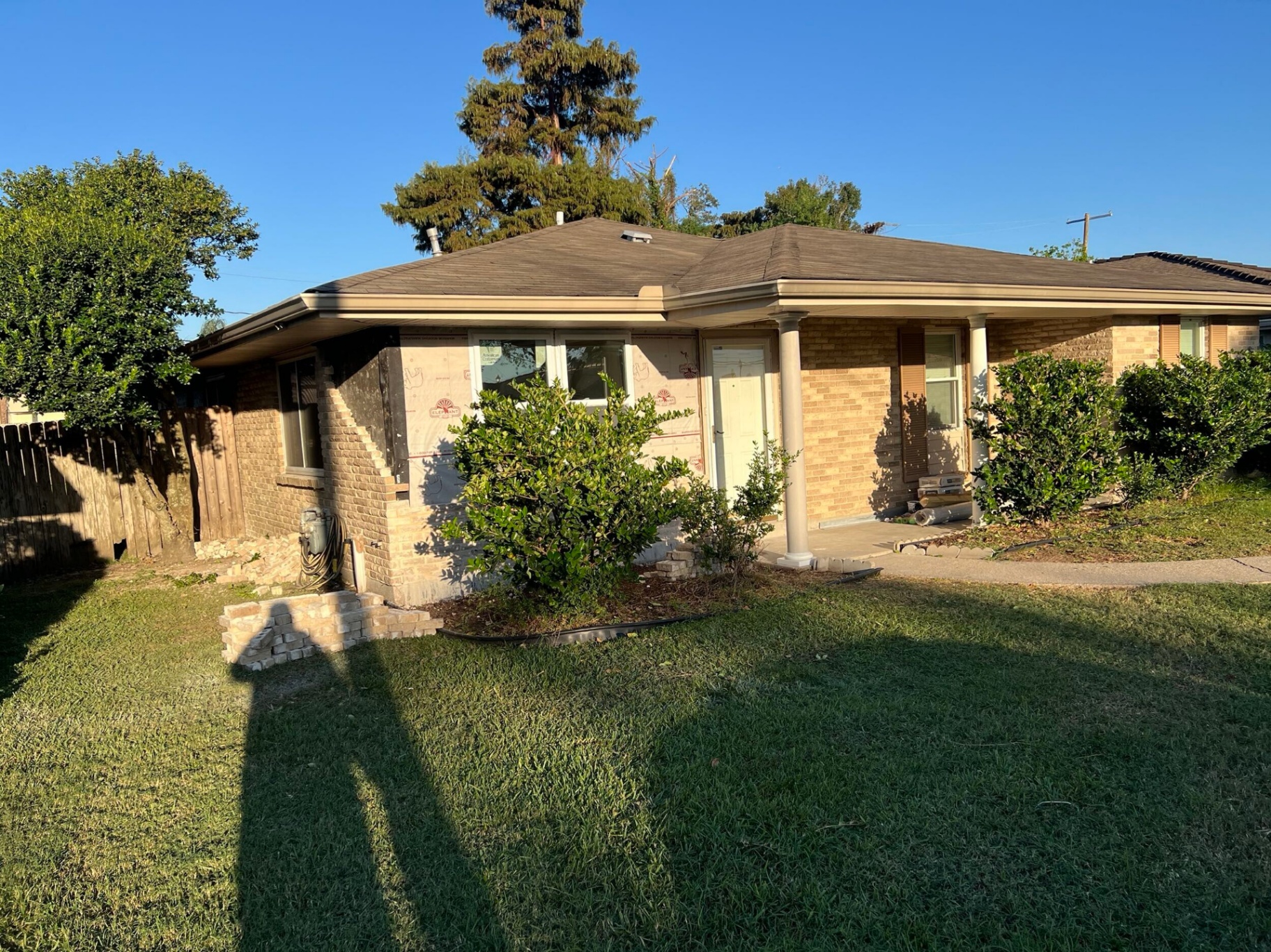 Exterior of the Gretna home with the front brick veneer nearly complete, new windows and roofline finished, homeowner's shadow in the foreground