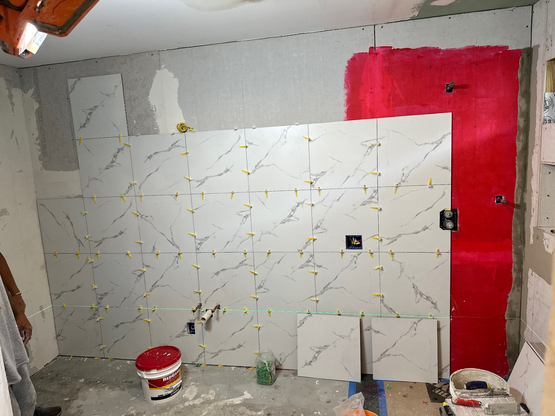 Marble-look large-format porcelain tile set on back shower wall with yellow leveling clips and laser line in Metairie master bath