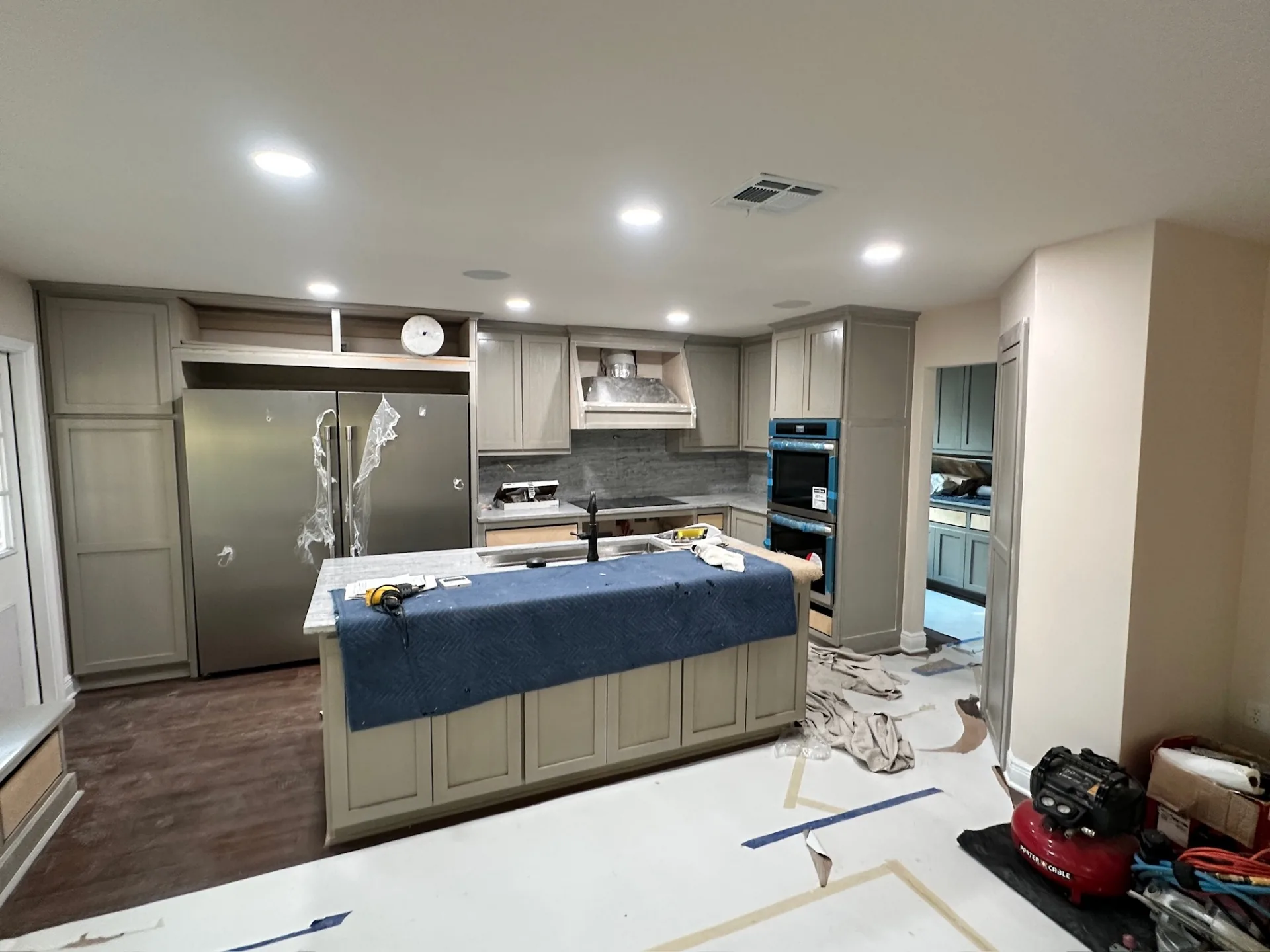 Kitchen at Blanke Street Metairie home with new recessed lighting, stainless range hood, wall ovens, and refrigerator installed on gray-stained shaker cabinetry